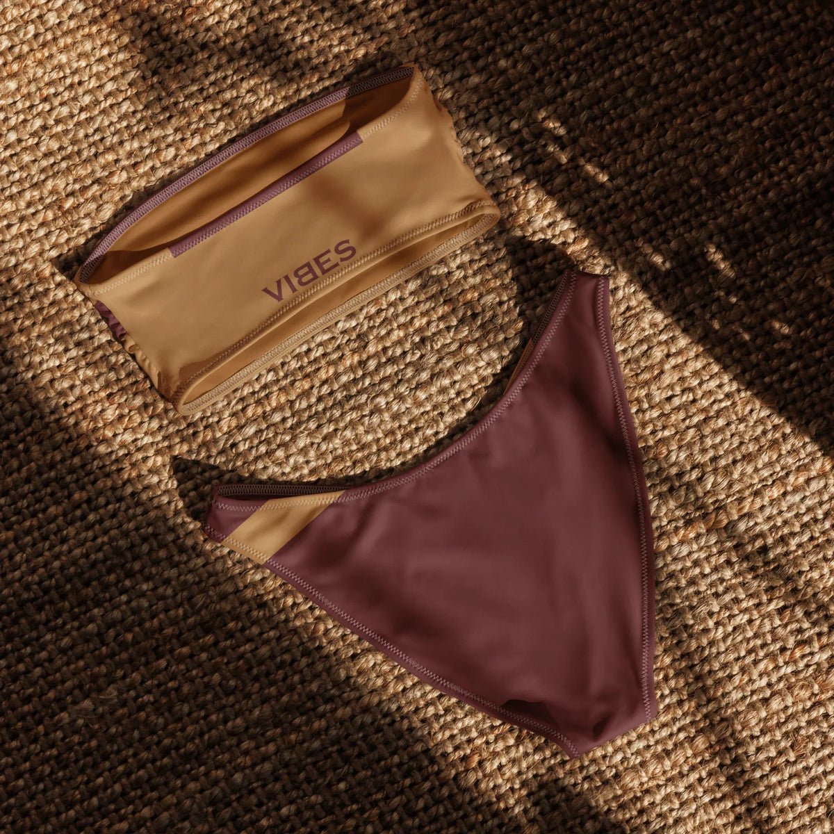 CREWILD Bandeau-Bikini in Braun und Weinrot auf einer Naturfaser-Unterlage.