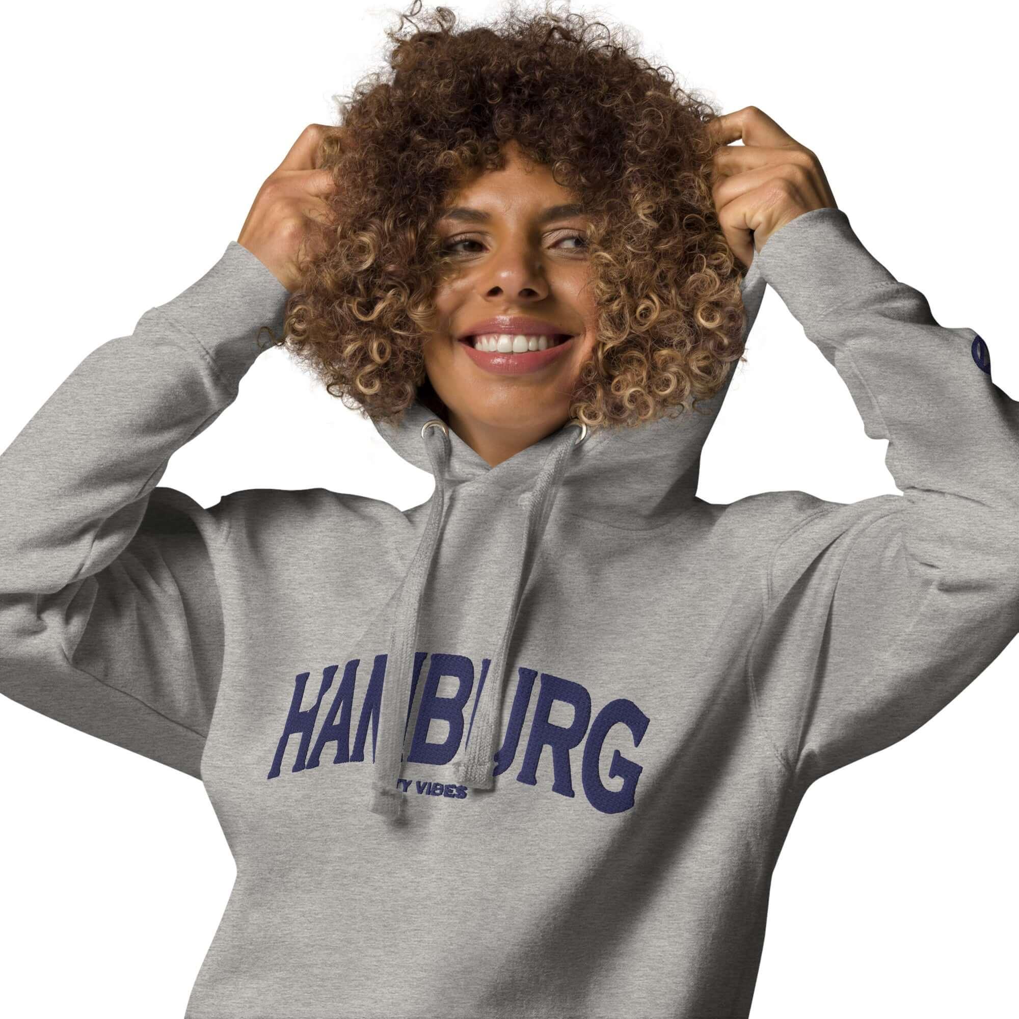 Frau trägt grauen CREWILD Unisex Hoodie mit blauem Hamburg-Schriftzug