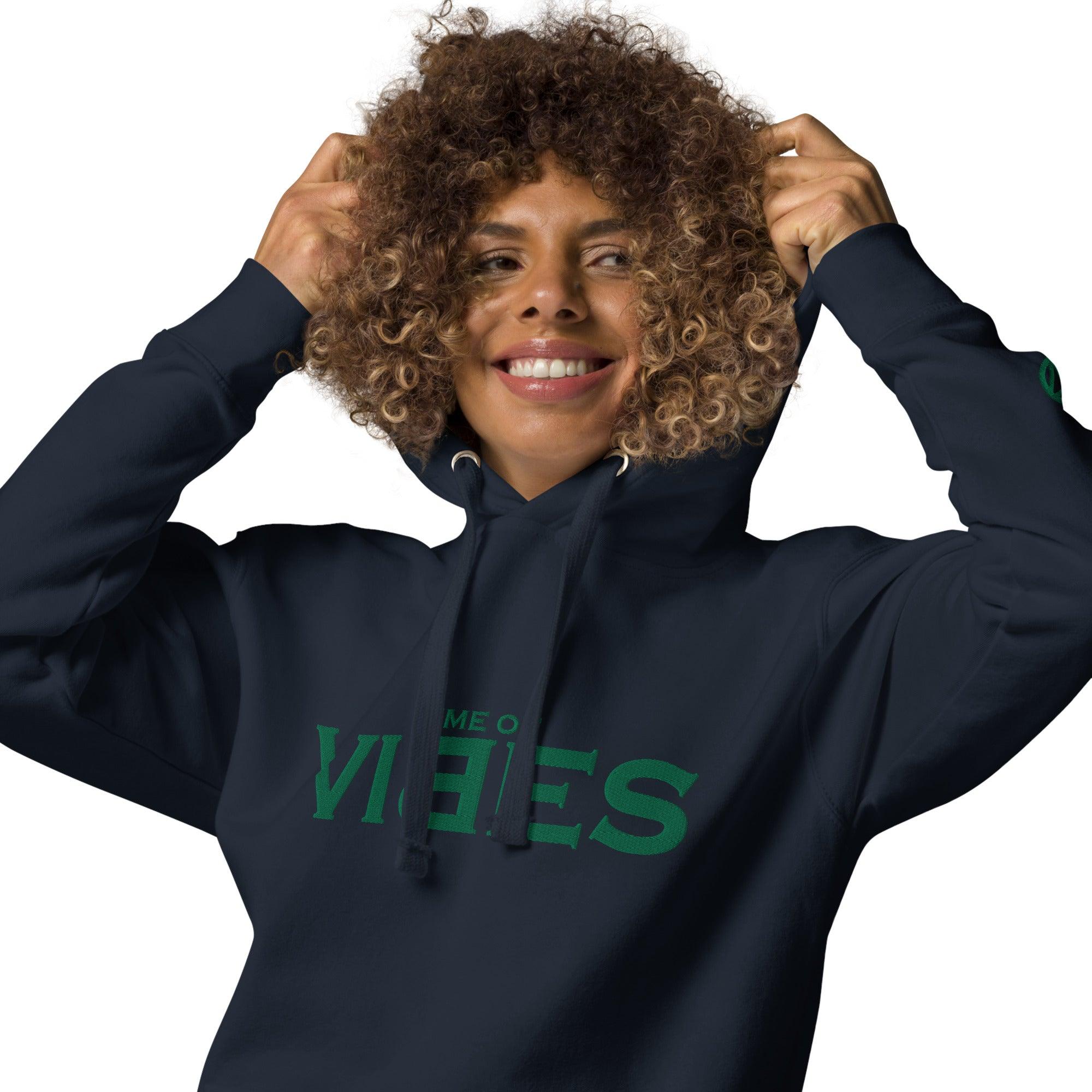 Frau mit lockigen Haaren trägt marineblauen Hoodie mit grünem Vibes Schriftzug, lächelt