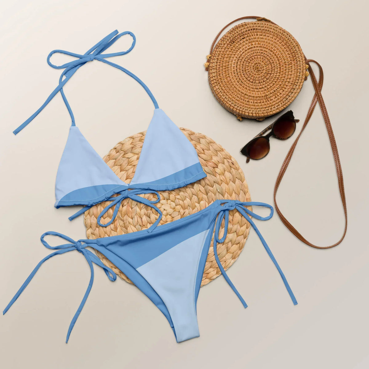 Hellblauer CREWILD Schnür-Bikini WAVES mit Sonnenbrille und Strohtasche auf hellem Hintergrund