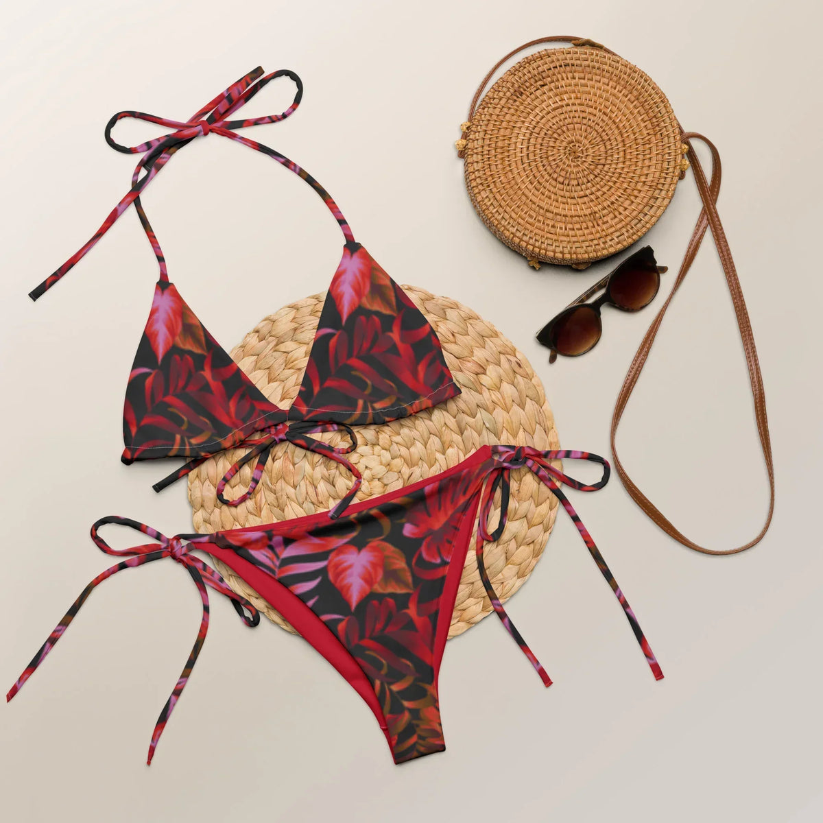 CREWILD Schnür-Bikini in Rot/Schwarz mit Blattmuster, Sonnenbrille und Strohtasche auf Strohmatte.