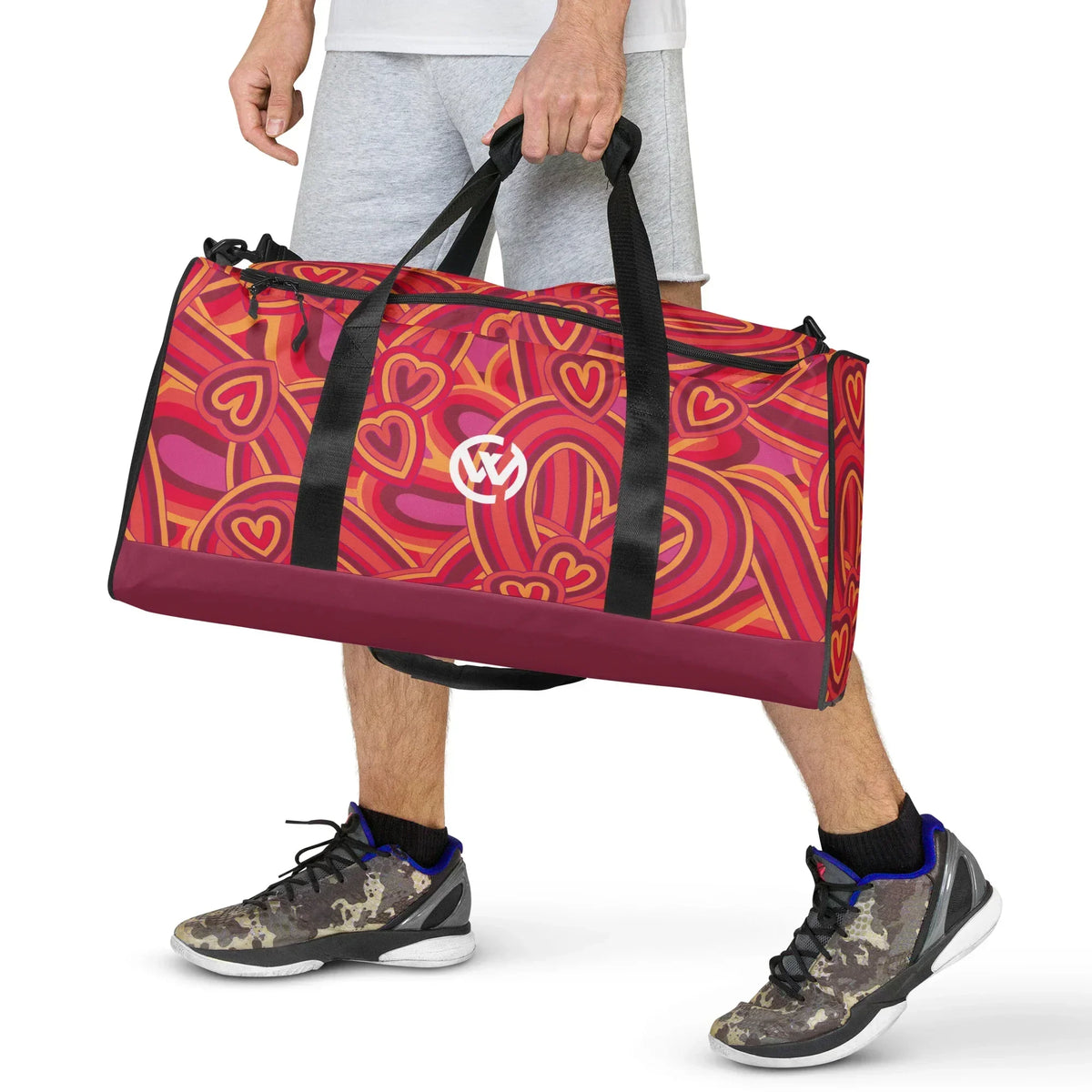 Person trägt eine sportliche Reisetasche mit buntem Herzmuster und Logo.