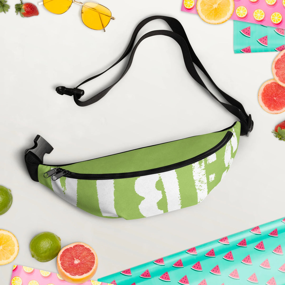 Grüne personalisierbare Bauchtasche mit weißem Aufdruck auf hellem Hintergrund mit Sommer-Accessoires