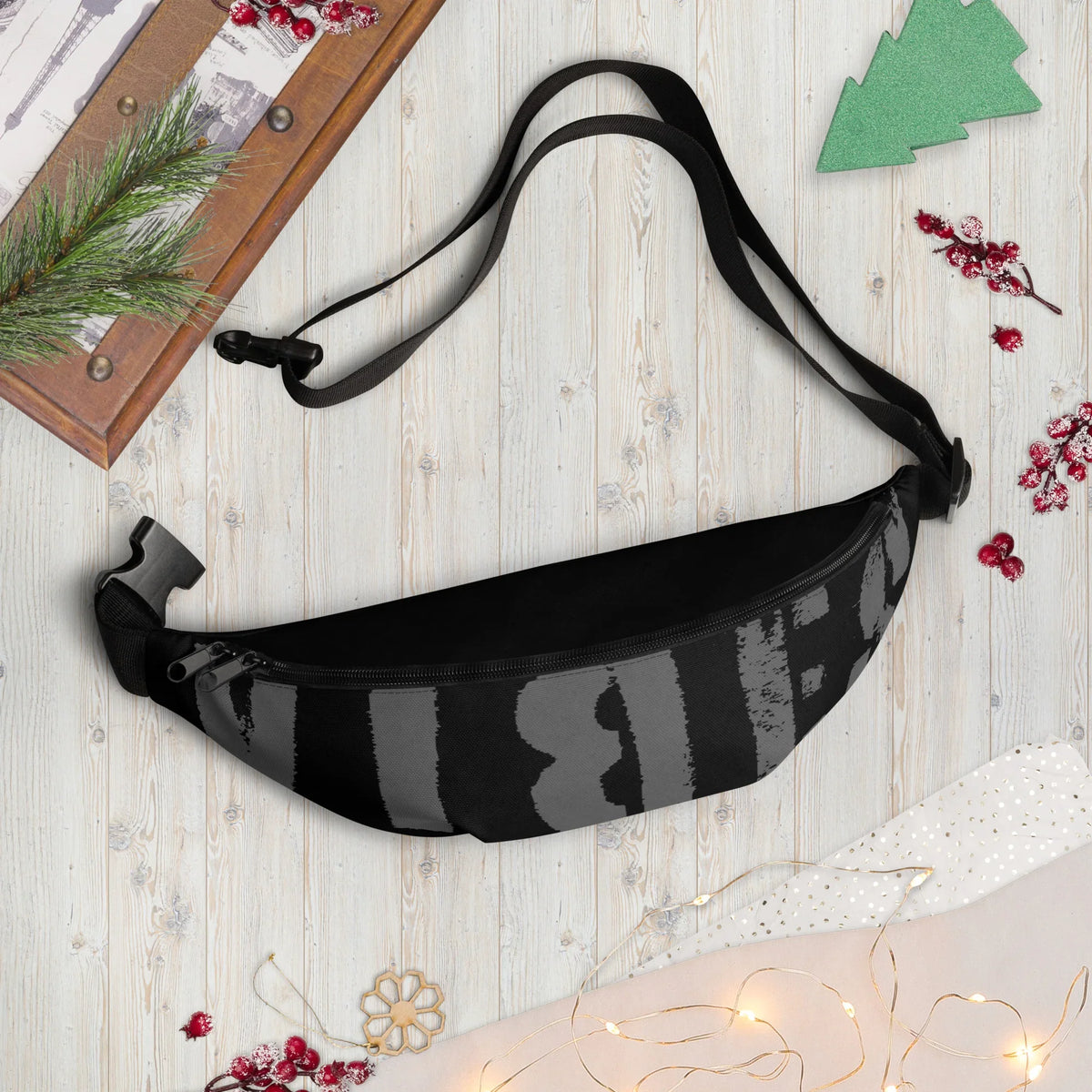 Schwarze Bauchtasche mit grauem Print auf hellem Holzhintergrund mit Weihnachtsdekoration