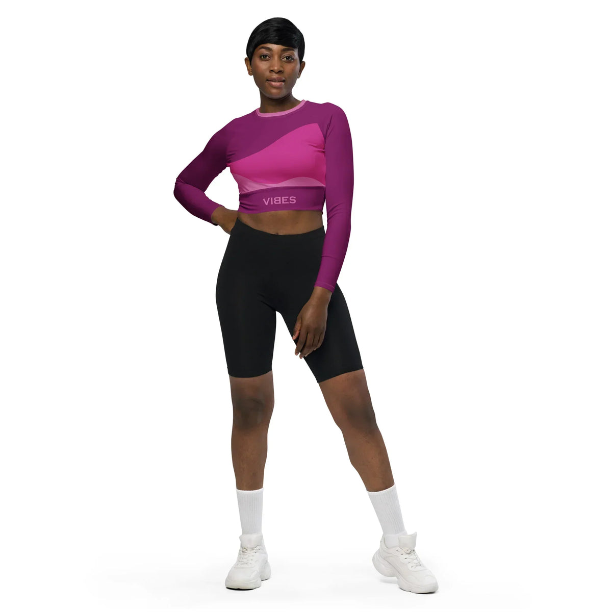 Frau trägt CREWILD Langarm Crop-Top in Pink mit abstraktem Muster und schwarze Shorts.