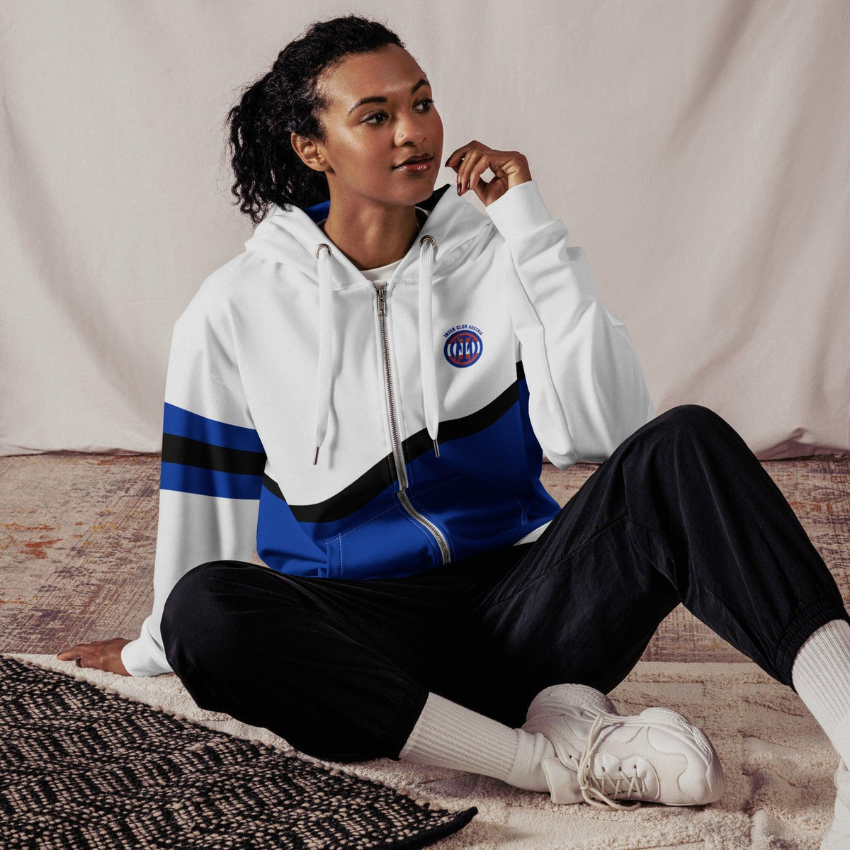 Frau trägt weißen CREWILD ICA Zip Hoodie mit blauem Design und schwarzen Jogginghosen.