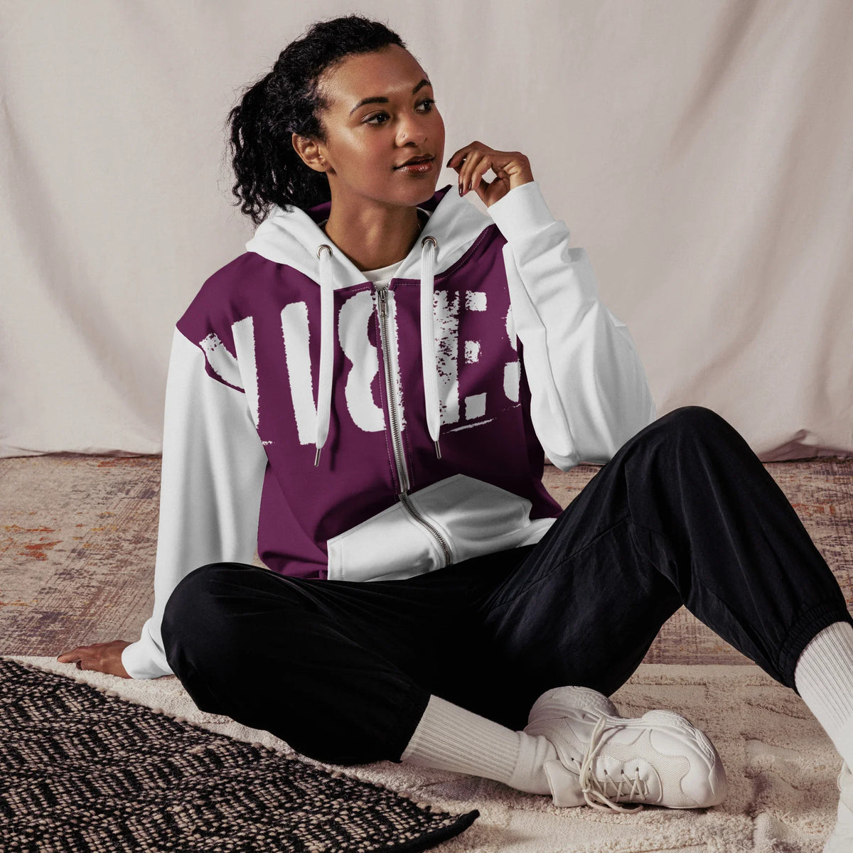 Person trägt einen weiß-violetten Hoodie mit Grafikprint und schwarze Jogginghose.