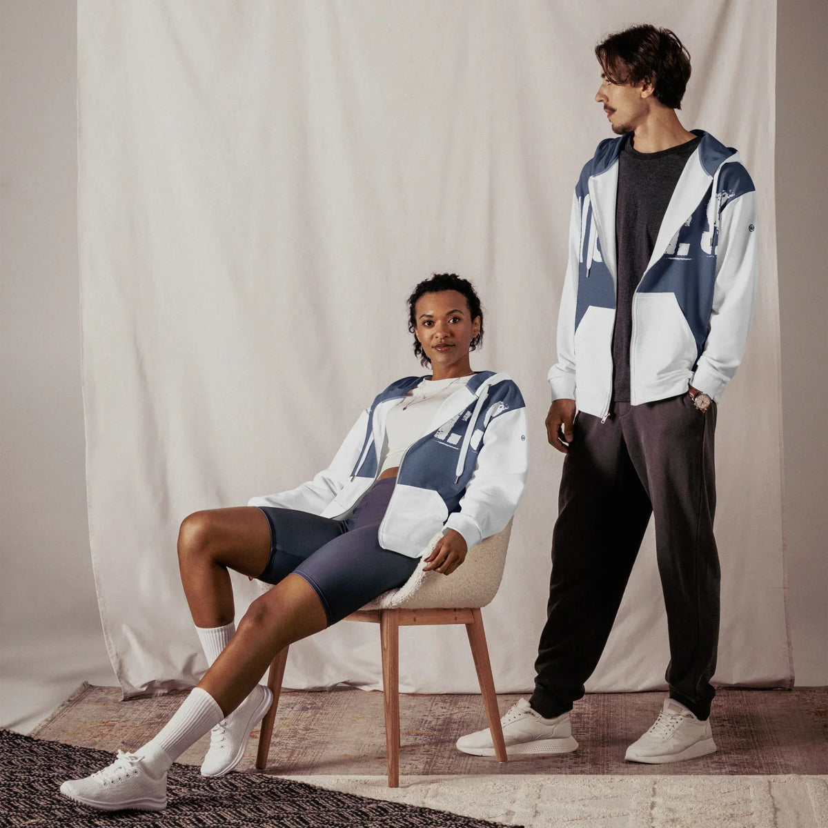 Zwei Personen tragen den blau-weißen CREWILD Zip-Hoodie in einem minimalistischen Studio.