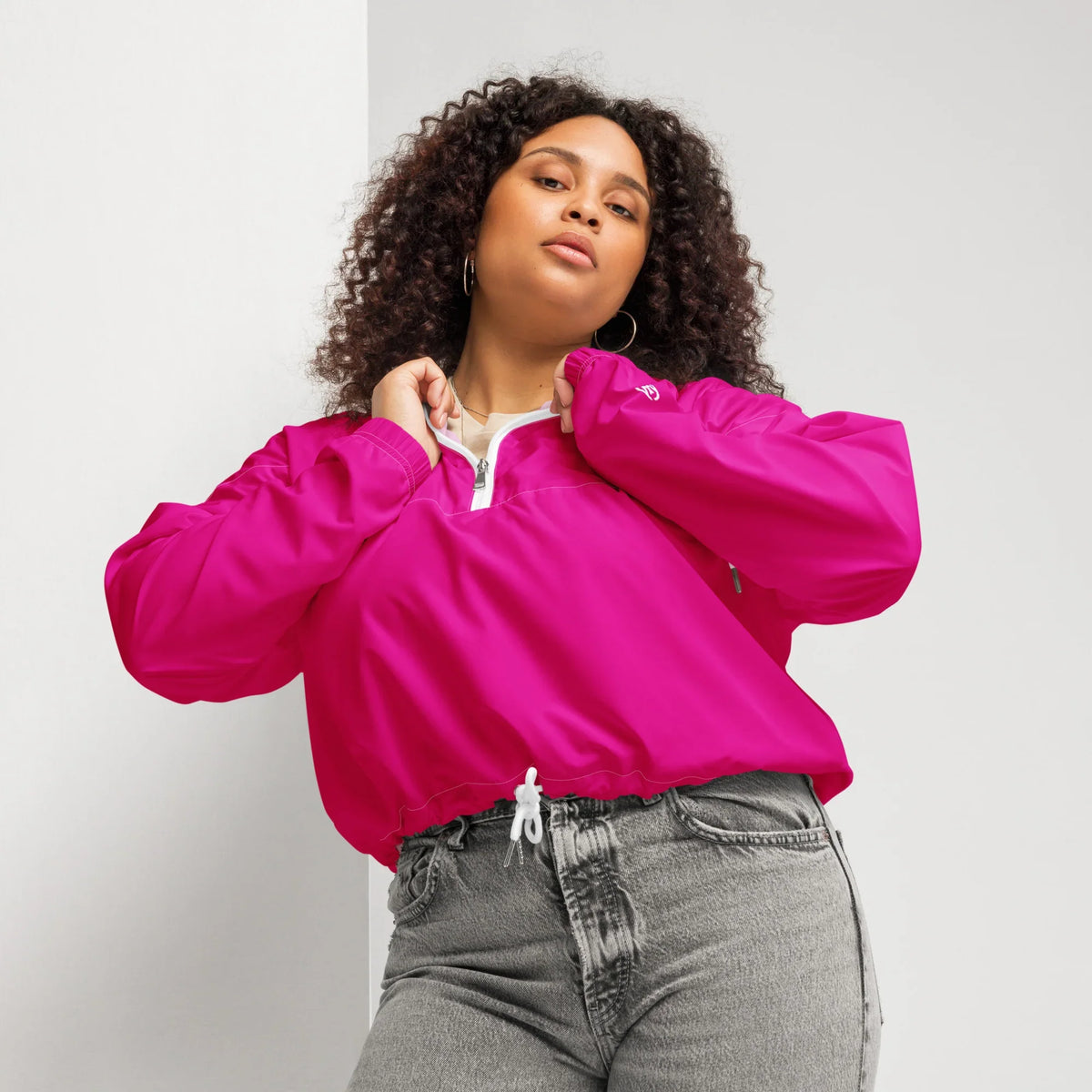 Frau mit lockigem Haar trägt eine pinke Windjacke und graue Jeans.