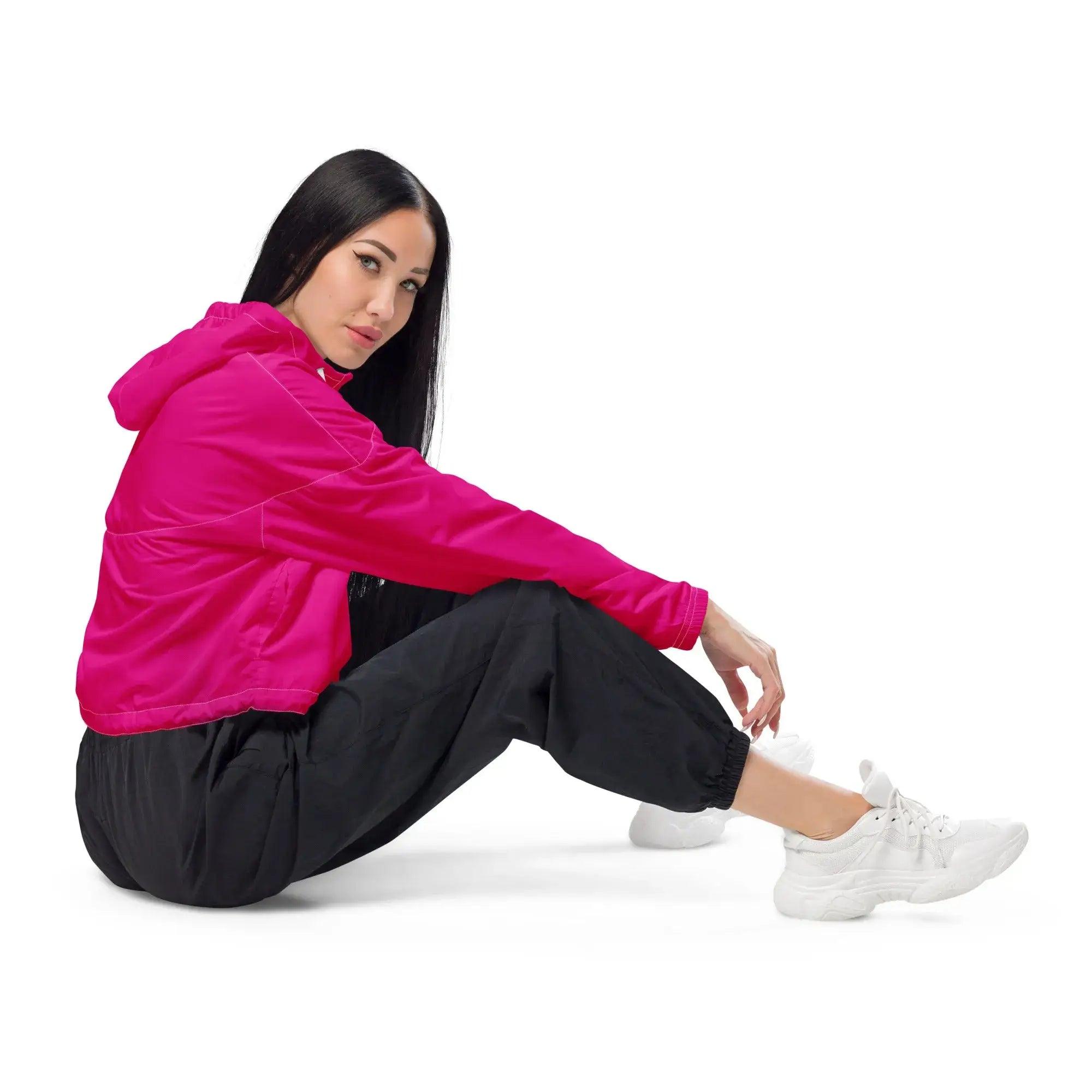 Frau mit pinker Cropped-Windbreaker Jacke, schwarzer Hose und weißen Sneakern auf weißem Hintergrund