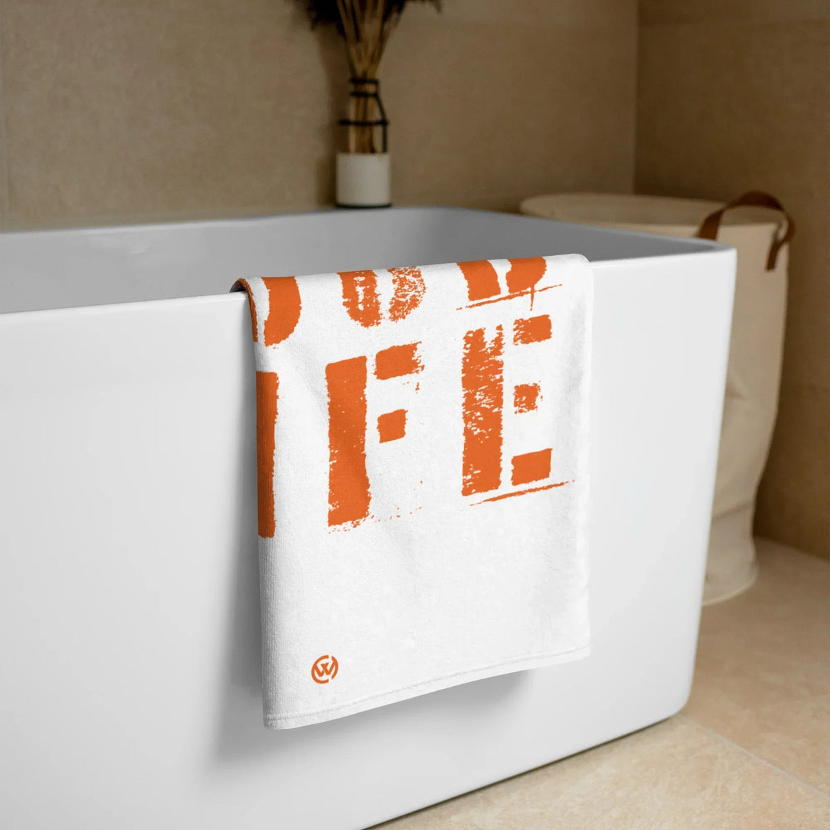 Weißes CREWILD Strandtuch mit orangefarbenem GOOD-LIFE Aufdruck über einem Badewannenrand.
