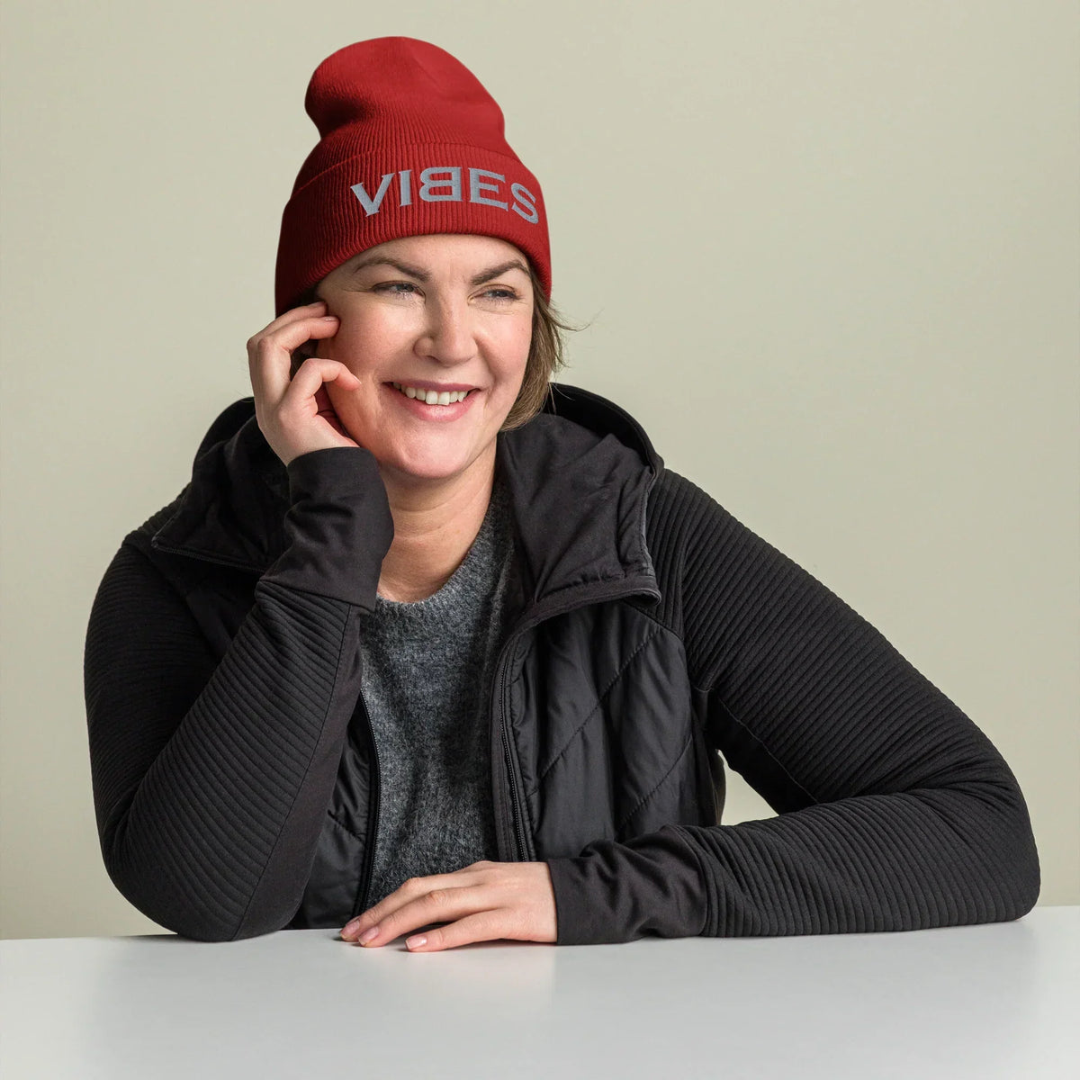 Lächelnde Frau mit einer roten CREWILD Beanie Mütze mit grauem VIBES-Stick.