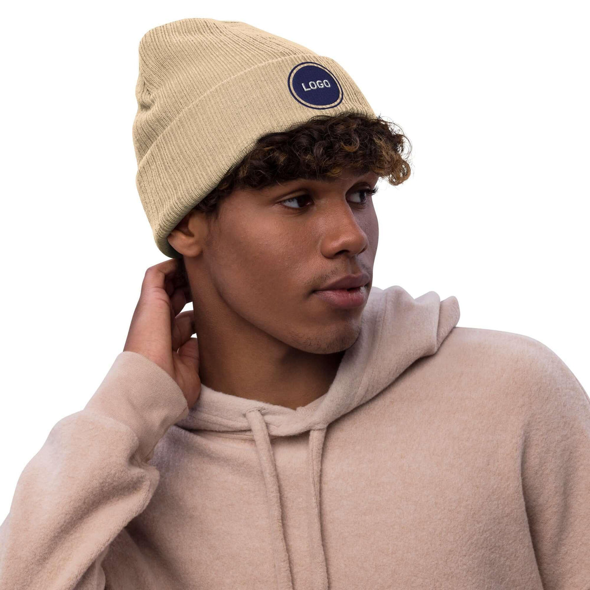 Beige Strickmütze mit Logo-Aufnäher, getragen von einem Mann im Hoodie