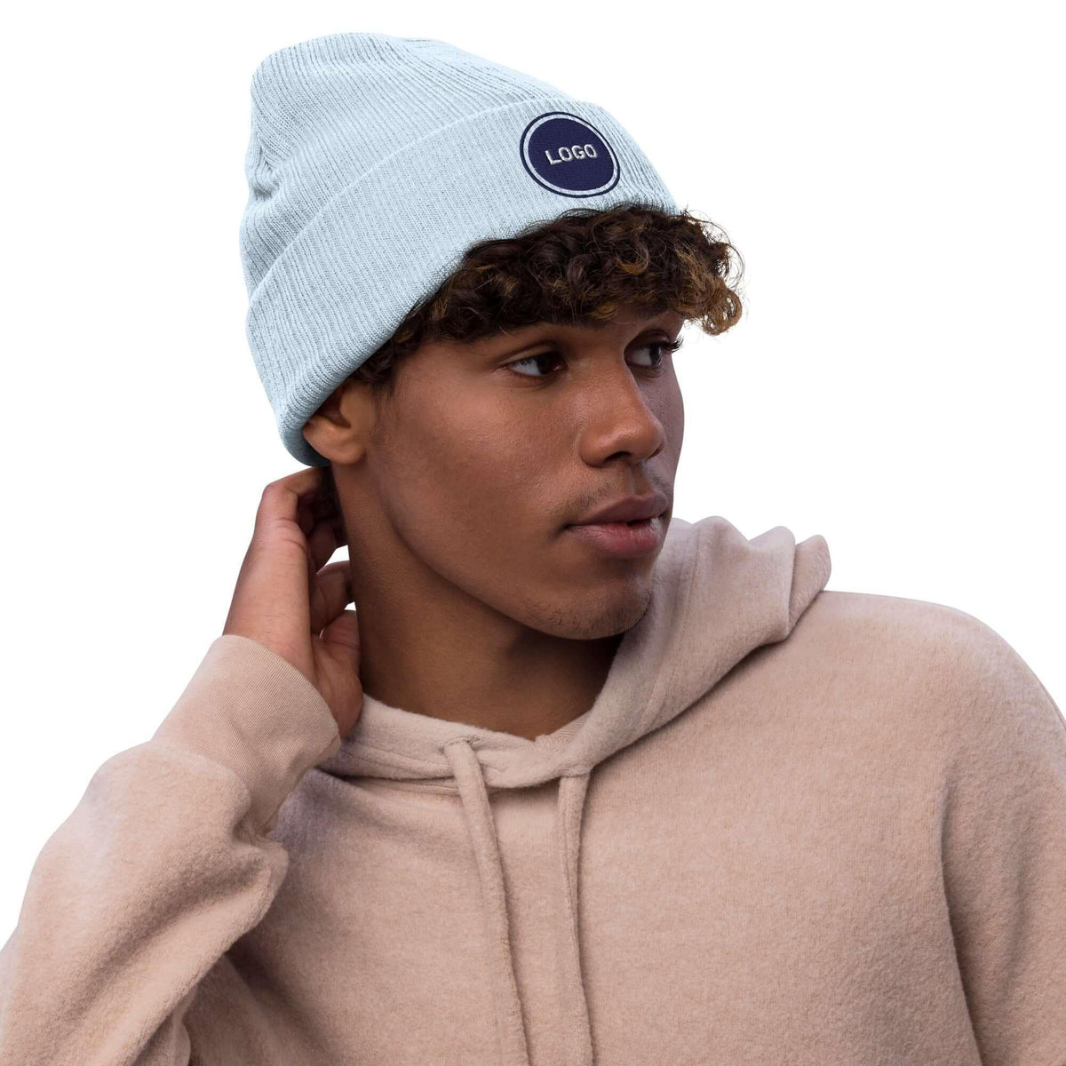 Hellblaue Strickmütze mit Logo-Patch und beige Hoodie an einem jungen Mann.