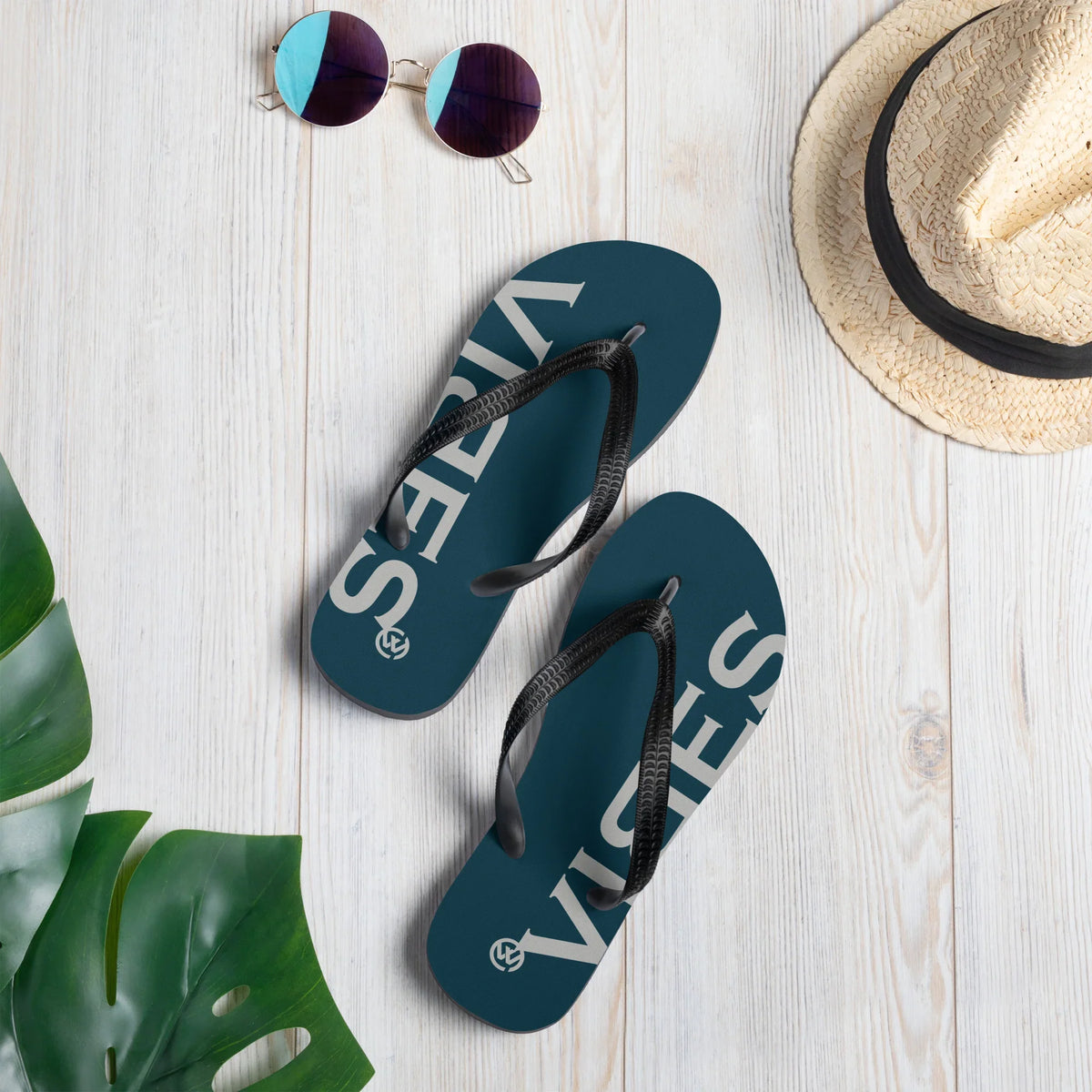 Blau-silberne CREWILD Flip-Flops mit VIBES-Schriftzug, Sonnenbrille und Strohhut auf hellem Holz.