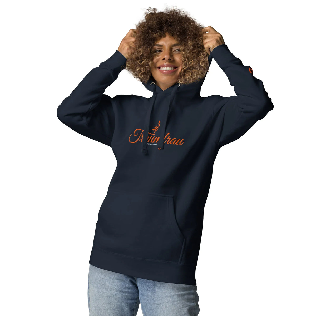 Lächelnde Frau mit lockigem Haar in einem dunkelblauen Hoodie mit orangefarbenem Aufdruck.