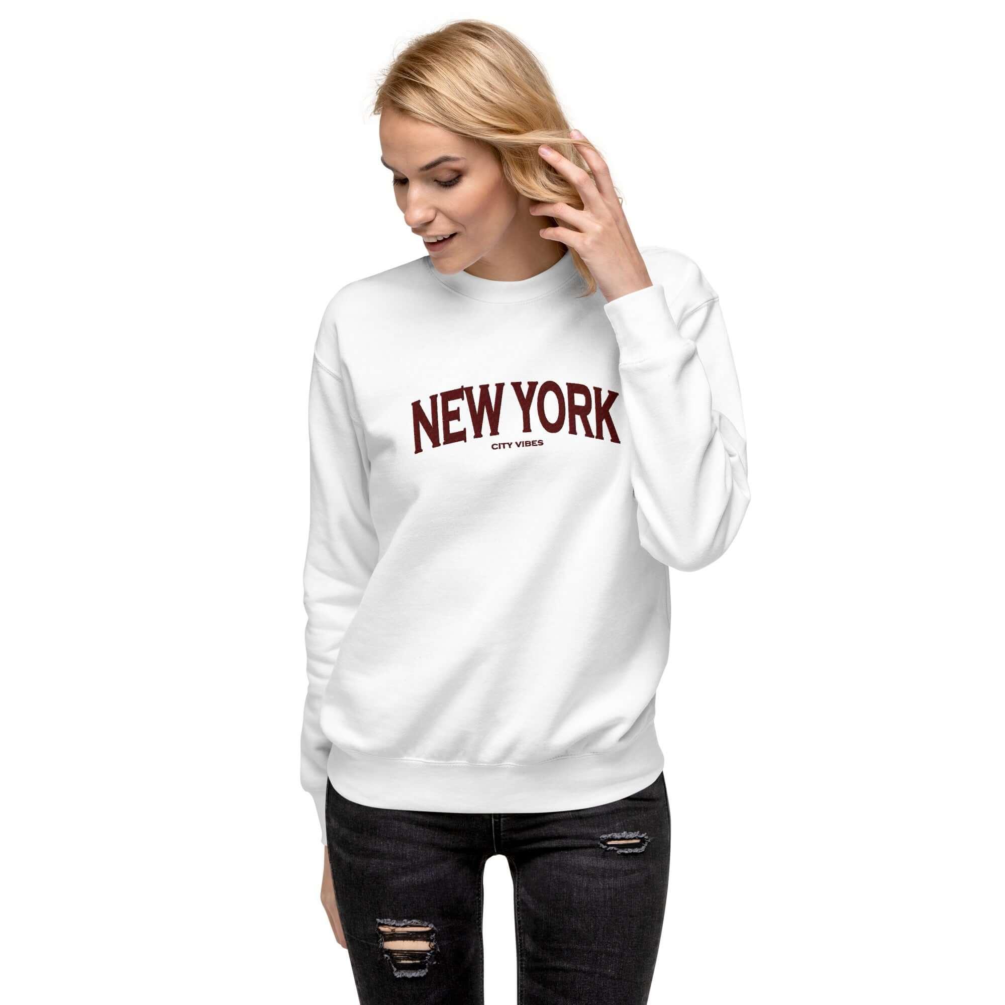 Frau in weißem Sweatshirt mit weinrotem New York City Vibes Aufdruck und schwarzen Jeans