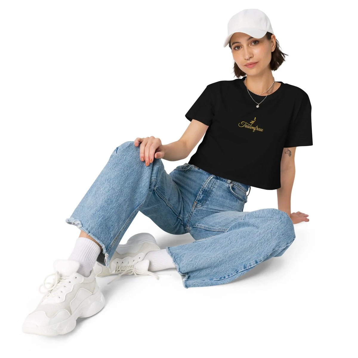 Frau in weißer Cap, Jeans und schwarzem CREWILD T-Shirt mit goldenem Traumfrau-Aufdruck.
