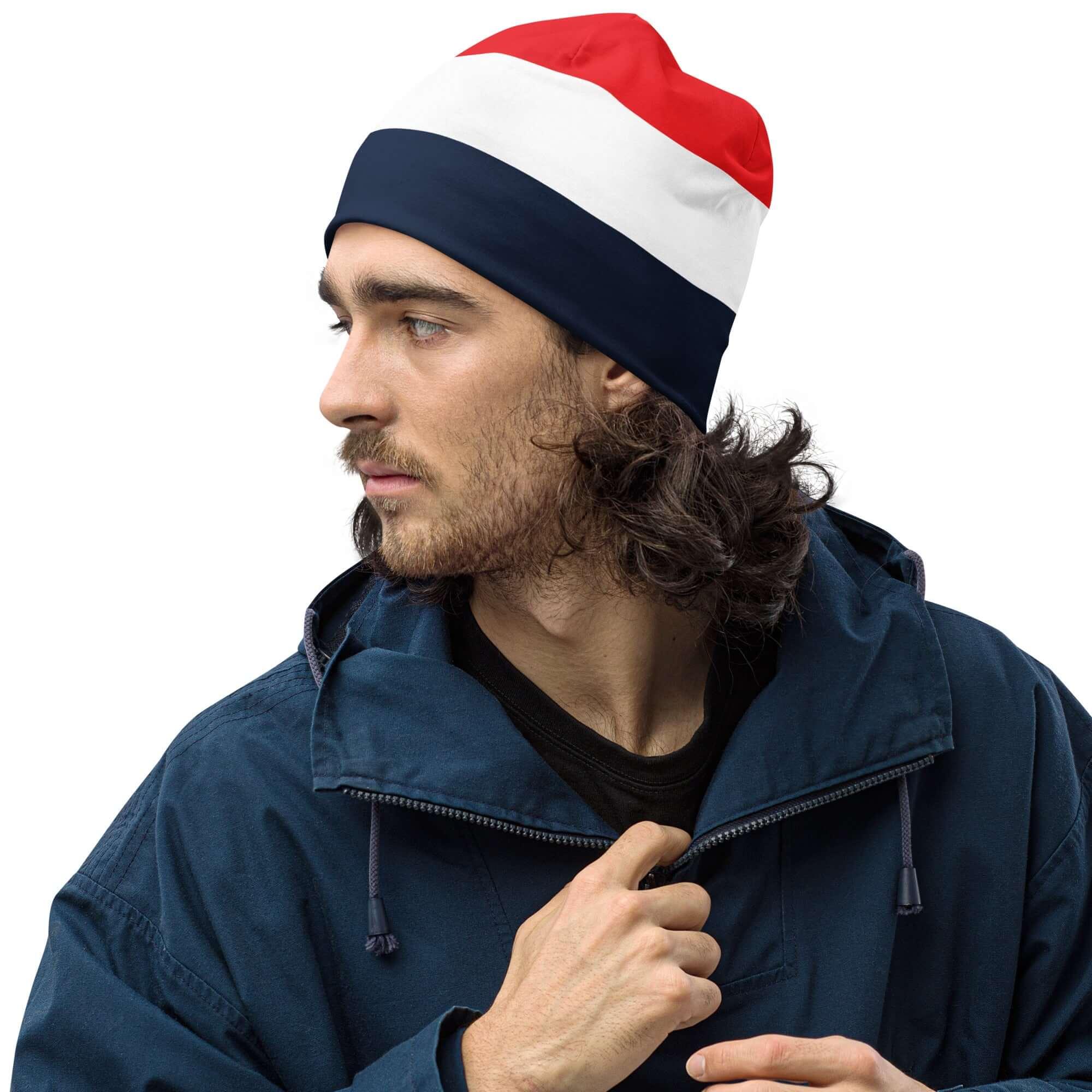 Mann mit Beanie in Rot-Weiß-Blau und blauer Jacke vor weißem Hintergrund
