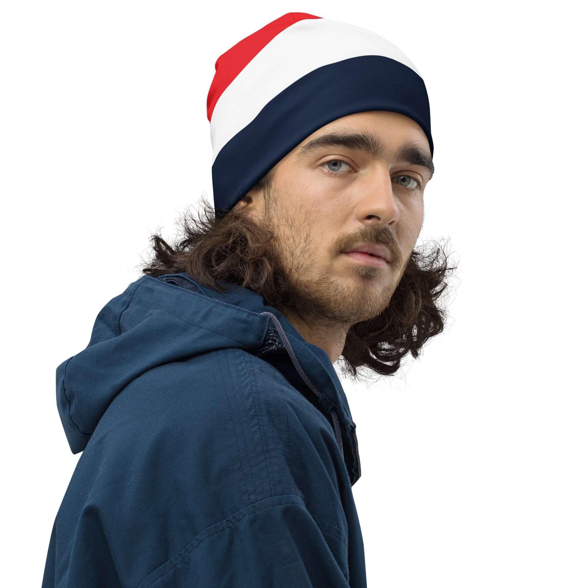 Mann mit langer dunkler Jacke trägt rot-weiß-blau gestreifte Beanie-Mütze