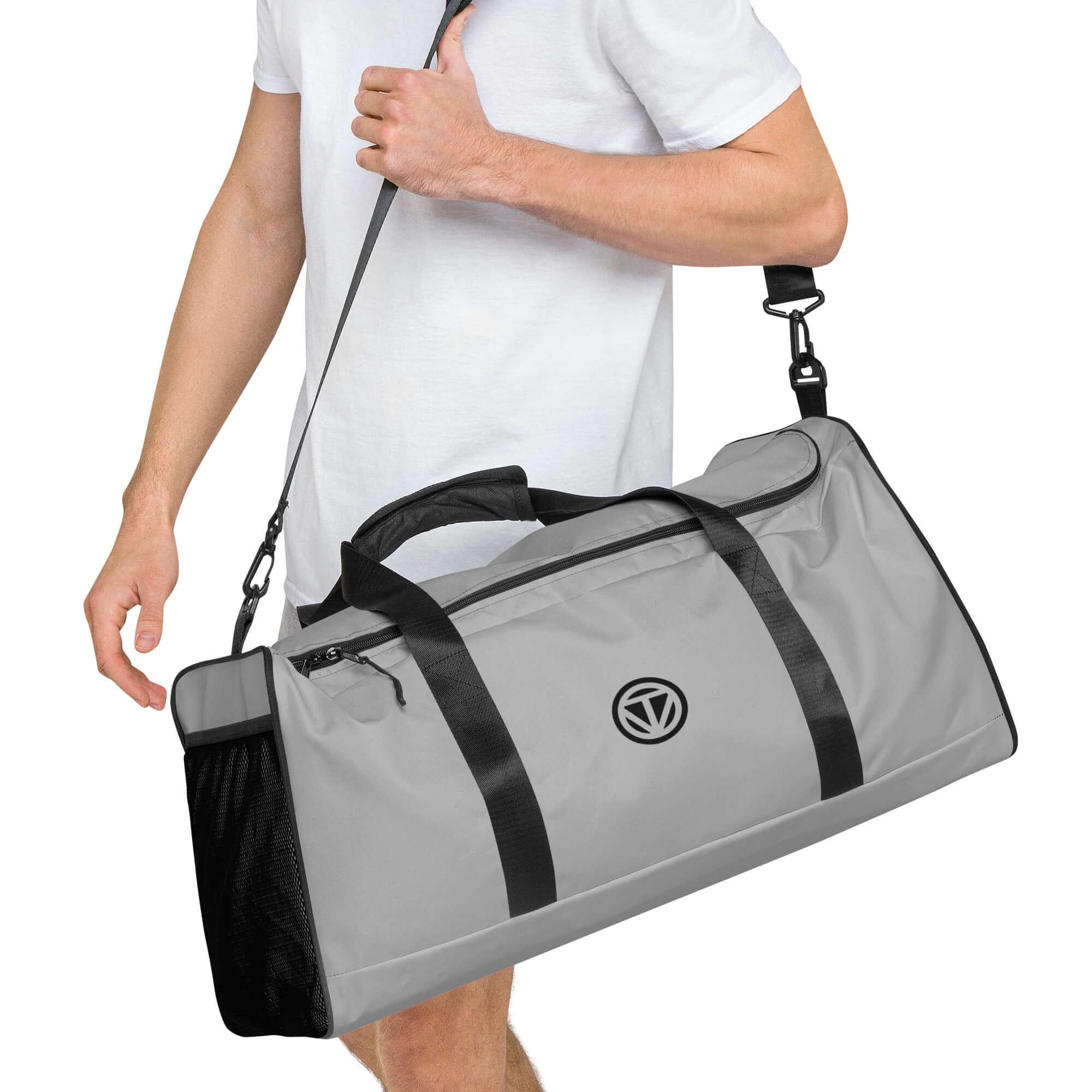 Graue Sporttasche mit schwarzem Logo, Schultergurt und Netz-Seitentasche, Mann trägt Tasche