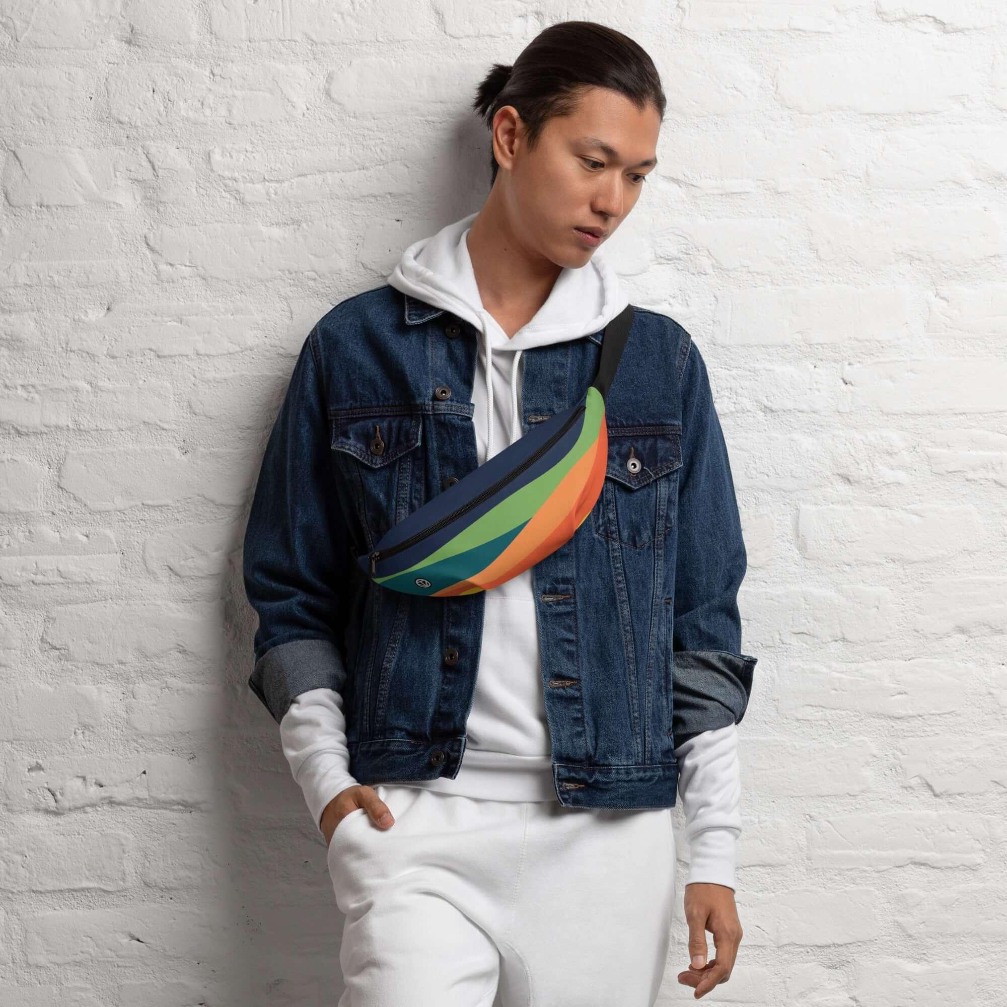 Mann mit bunter Bauchtasche, Jeansjacke und weißem Hoodie vor weißer Ziegelwand