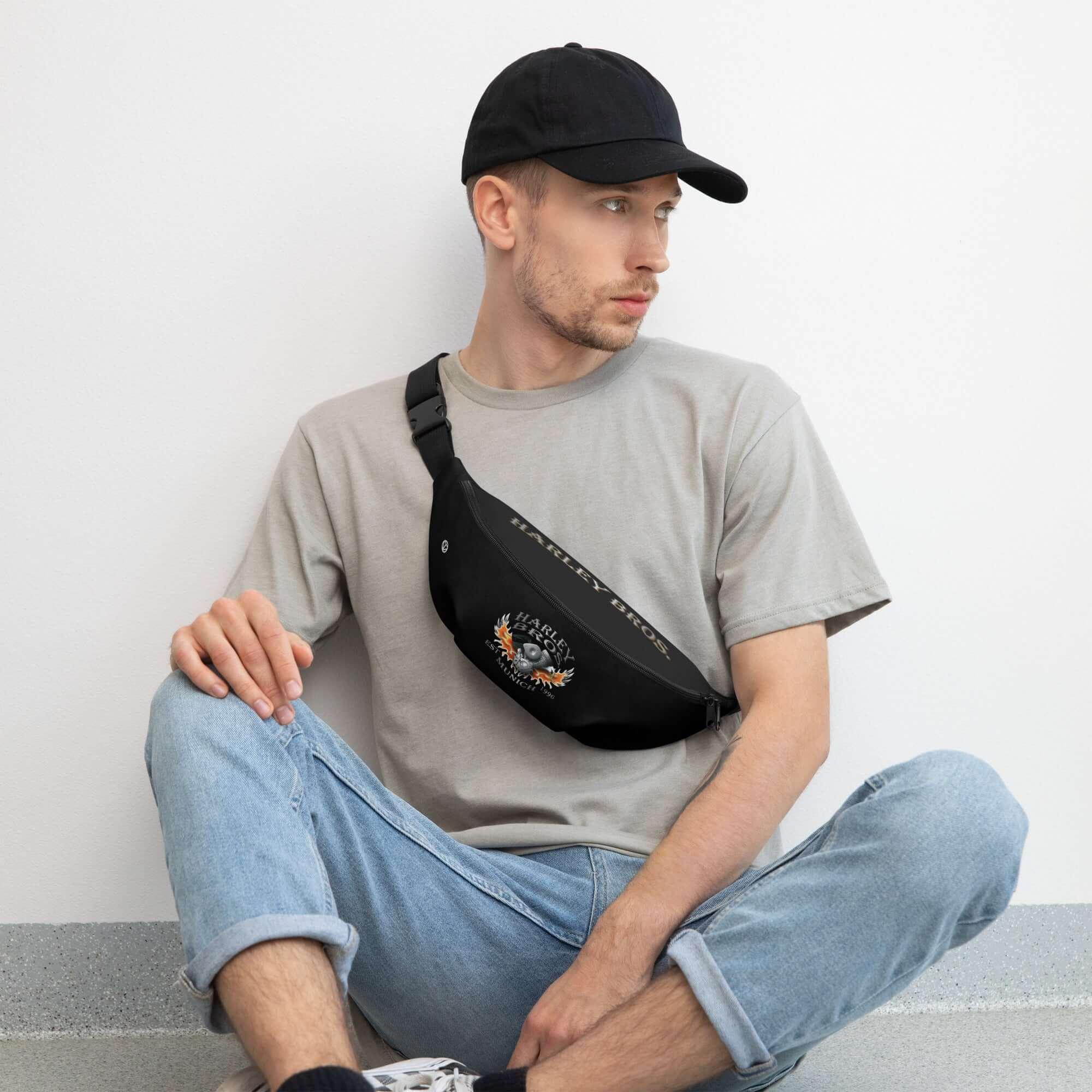 Mann mit schwarzer Bauchtasche und Baseballcap, sitzt leger vor weißer Wand, Streetwear Mode