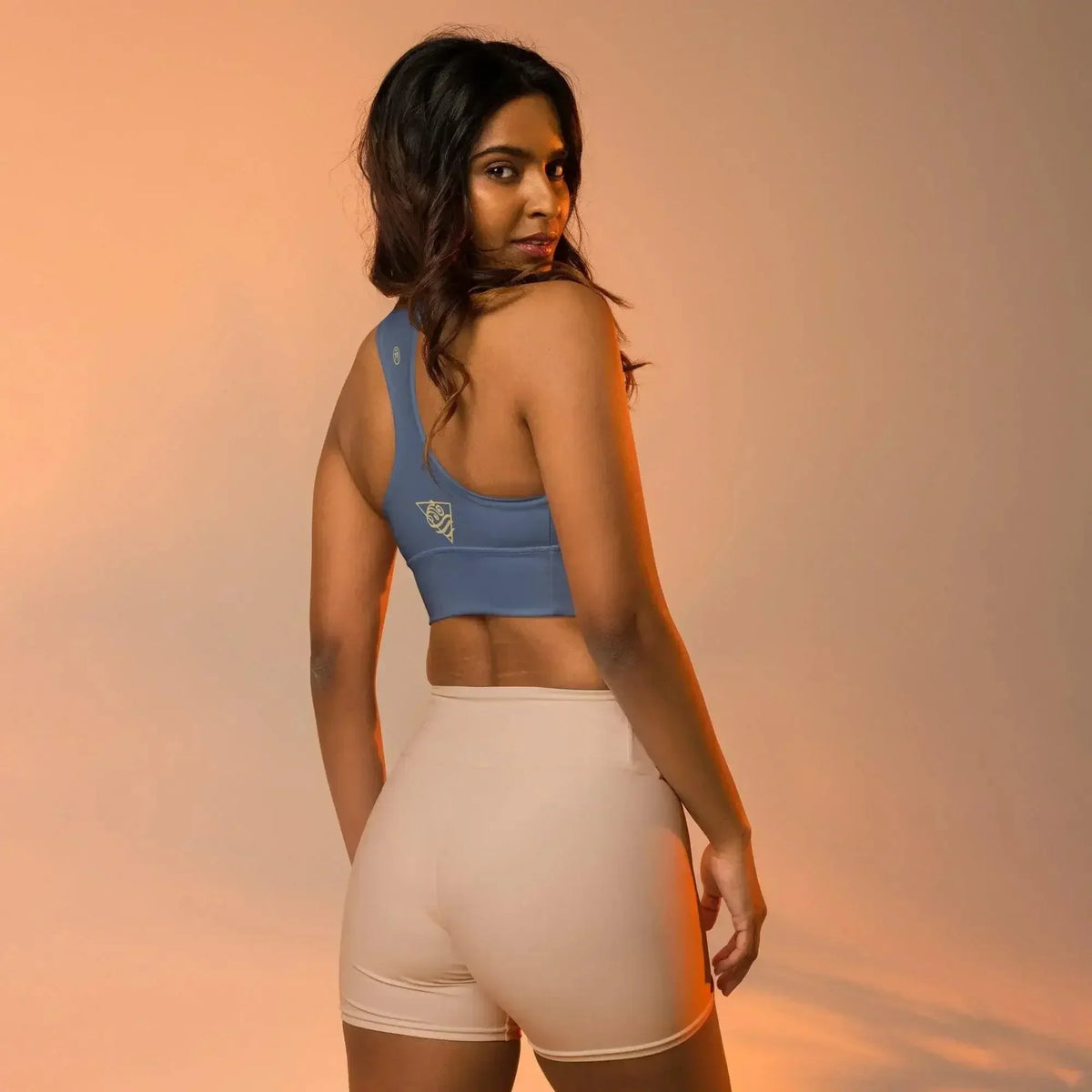 Frau in hellblauem CREWILD Sport BH und beigen Shorts in Seitenansicht.