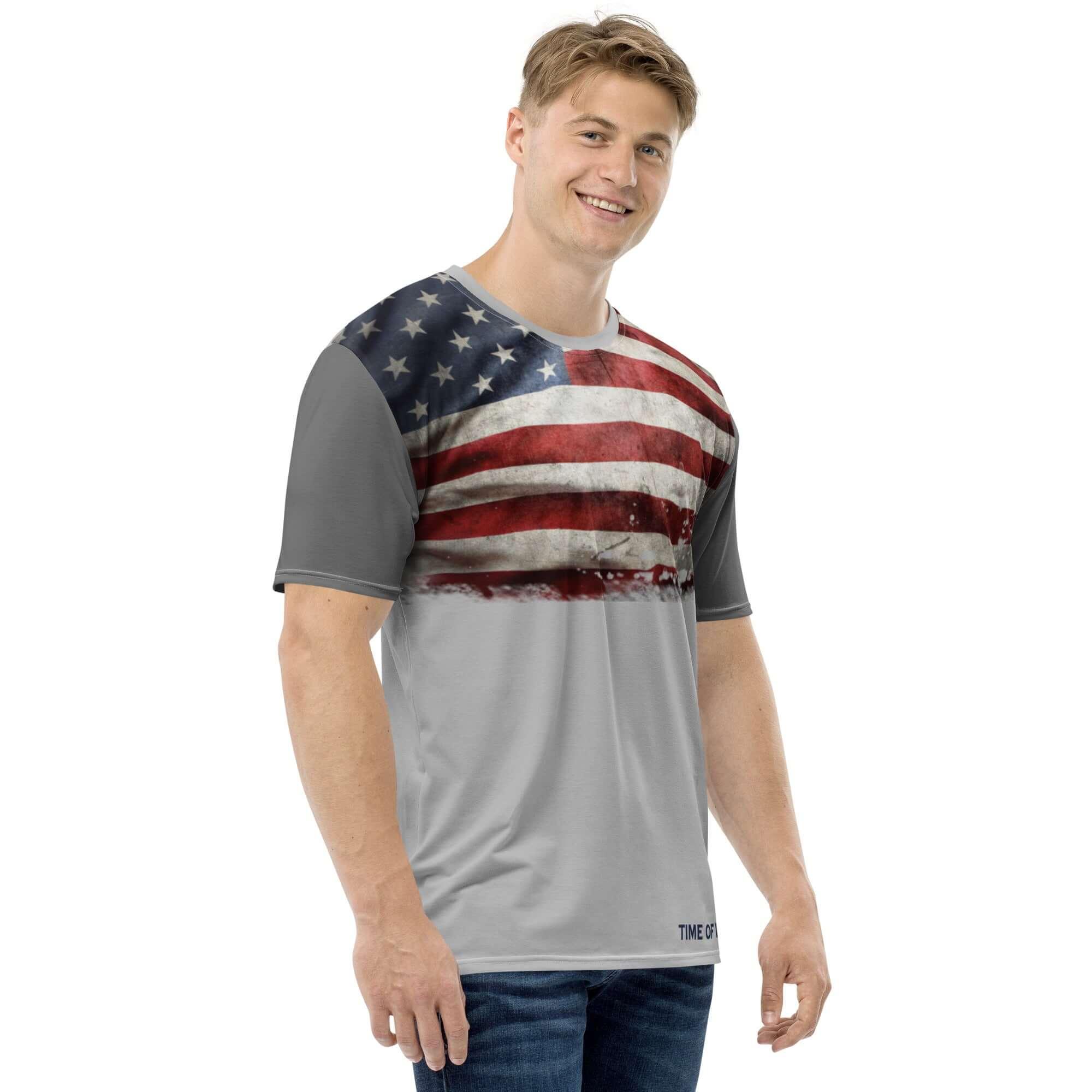 Mann trägt graues T-Shirt mit USA-Flaggen-Design, steht vor weißem Hintergrund.