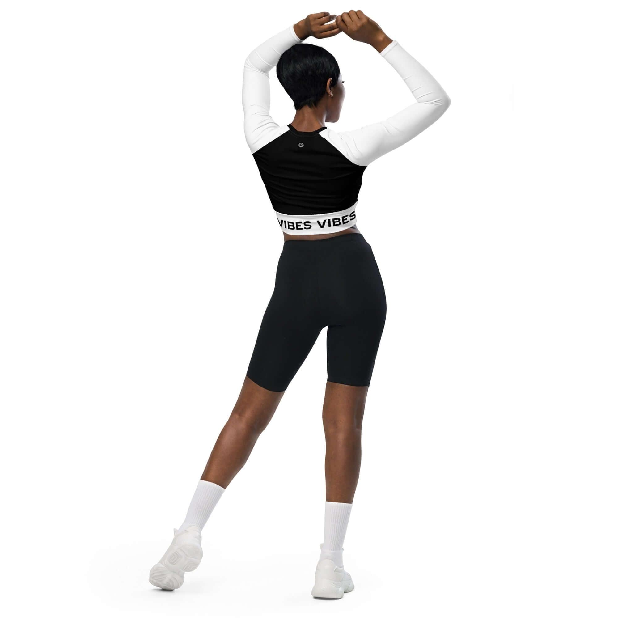 Frau trägt langärmliges Crop-Top mit Vibes-Schriftzug, schwarze Leggings, sportlich, Rückansicht