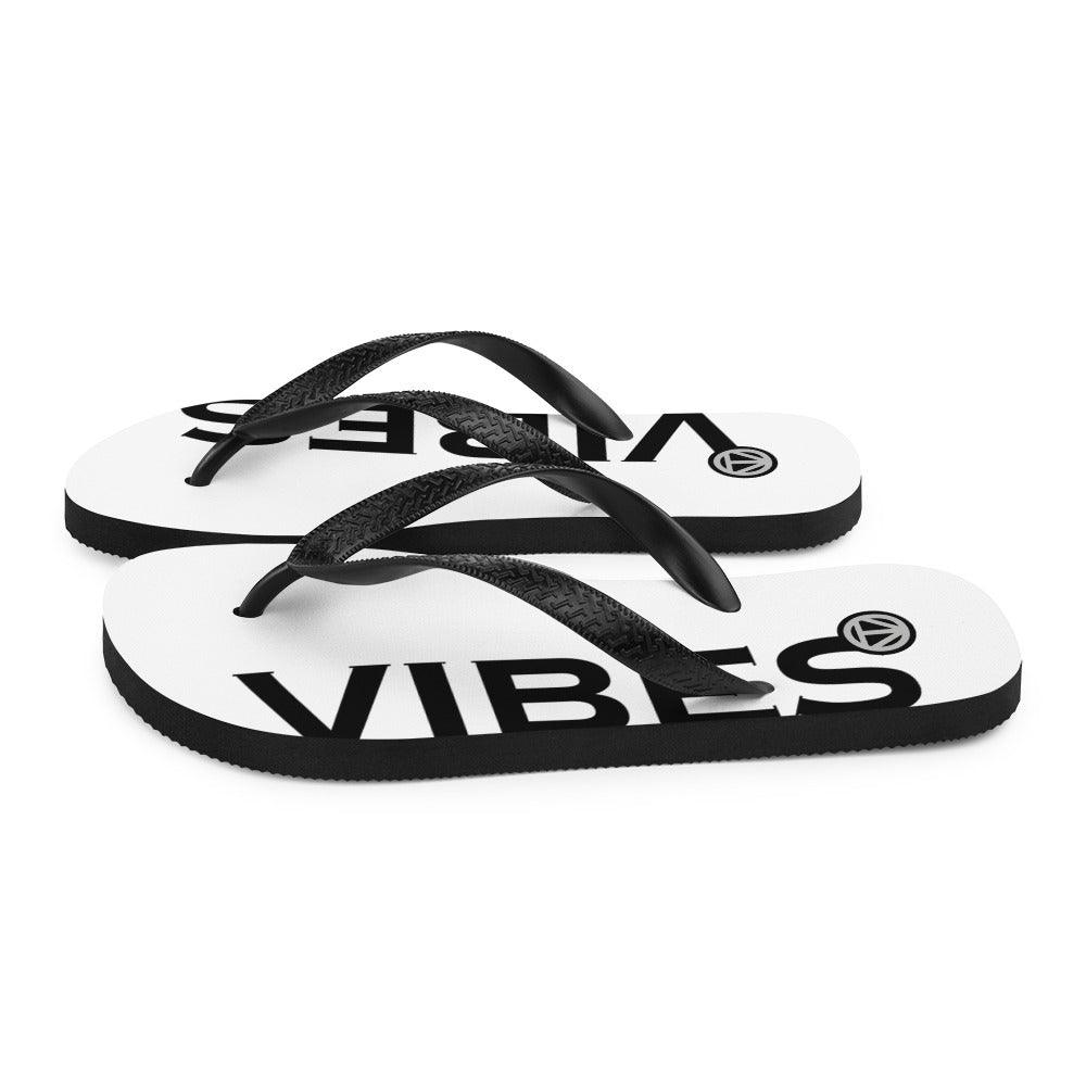 Weiße Flip Flops mit schwarzem Vibes Print und schwarzen Riemen auf weißem Hintergrund