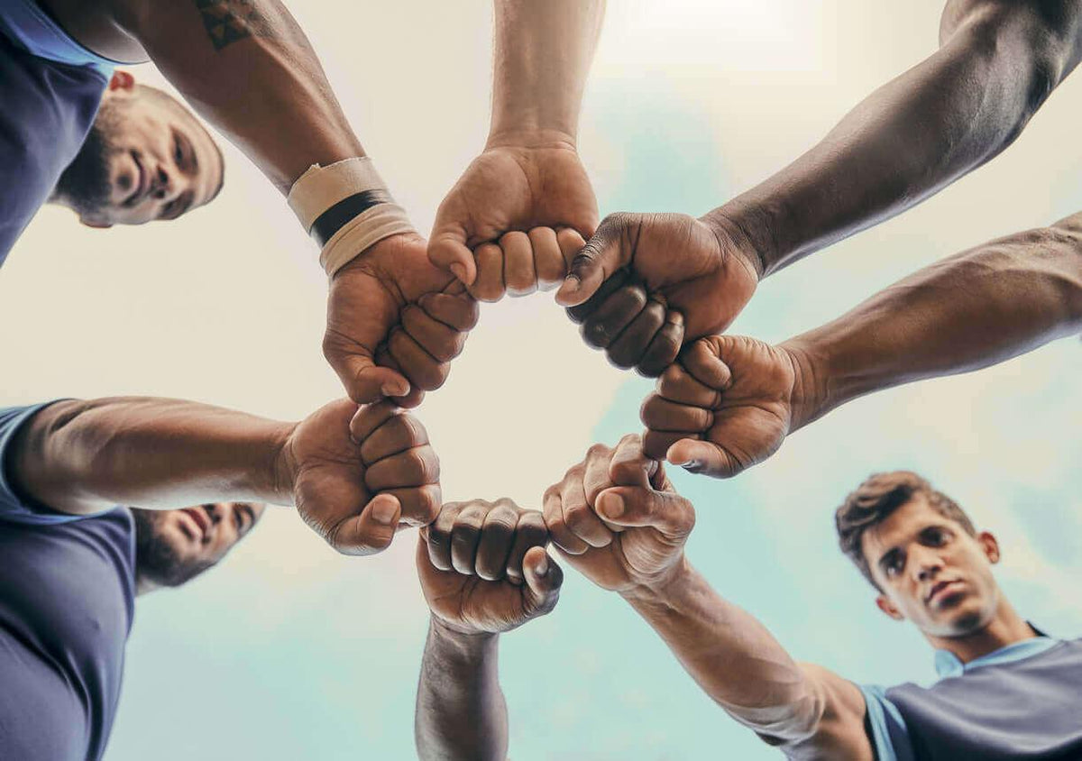 Mehrere Sportler mit Fäusten bilden einen Kreis, Teamwork, Gemeinschaft, Zusammenhalt im Freien.