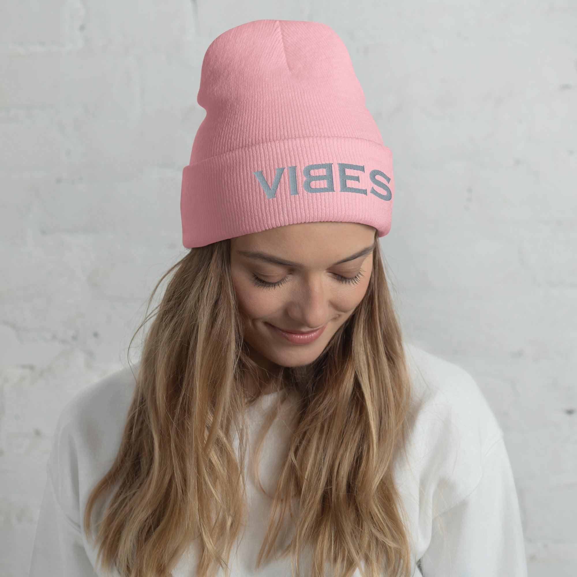 Frau mit rosa Beanie Mütze VIBES Aufdruck, weißer Pullover, vor heller Wand