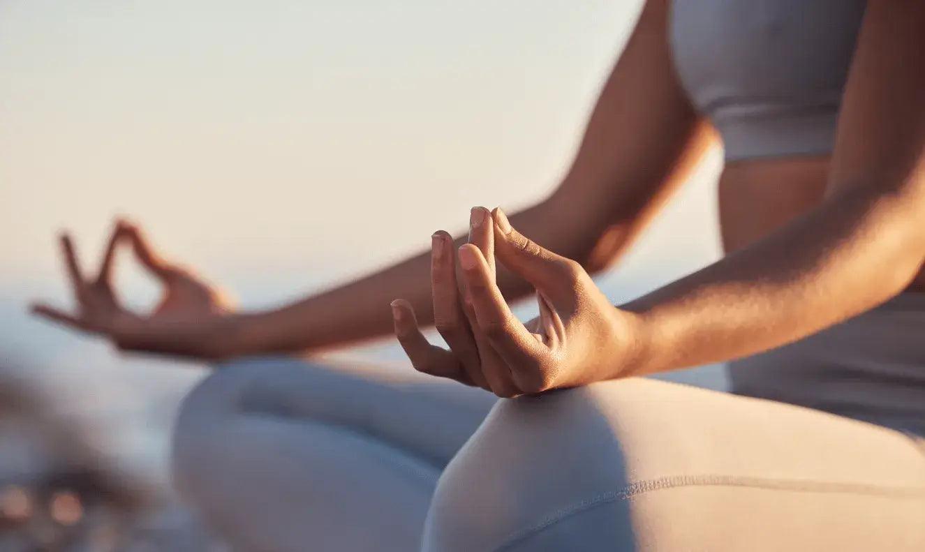 Frau macht Yoga im Freien, sitzt im Schneidersitz, meditiert bei Sonnenaufgang