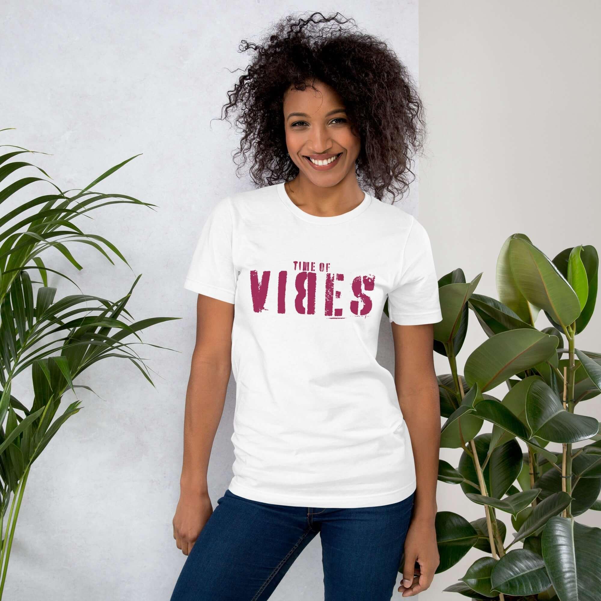 Frau mit Afro trägt weißes VIBES T-Shirt, steht entspannt neben grünen Zimmerpflanzen