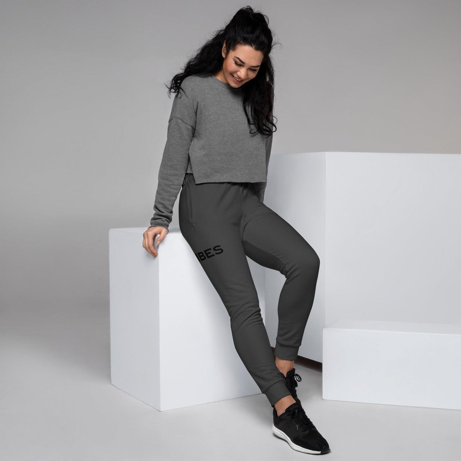 Frau trägt graues Cropped-Top und schwarze Jogginghose mit Vibes-Print, Mode Studiofoto