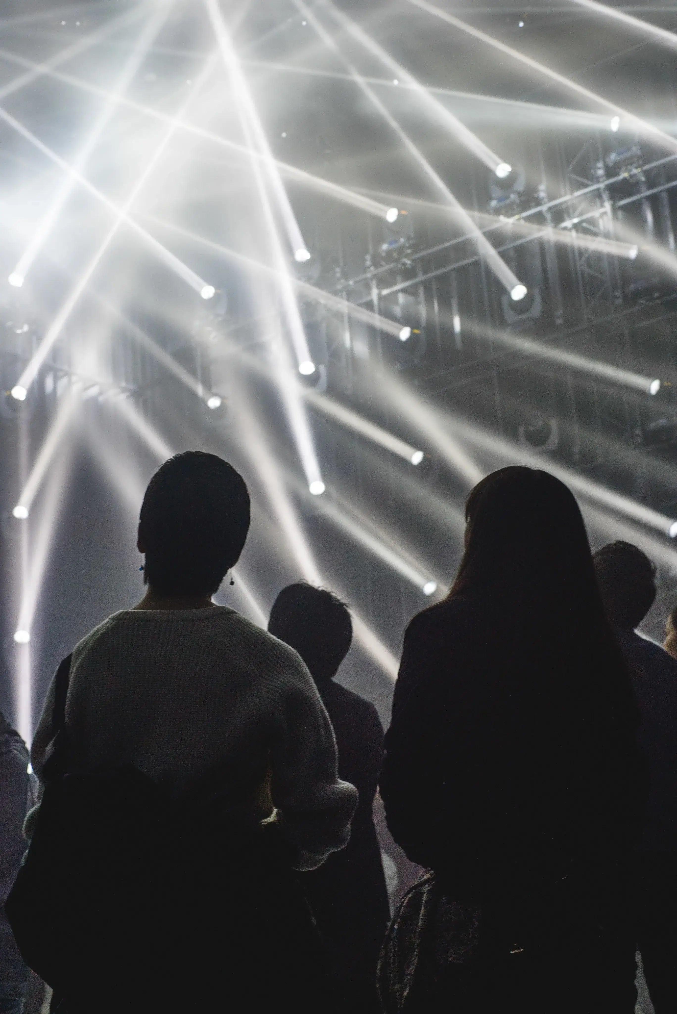 Menschen auf Konzert mit hellen Lichtern und Bühnenbeleuchtung im Hintergrund