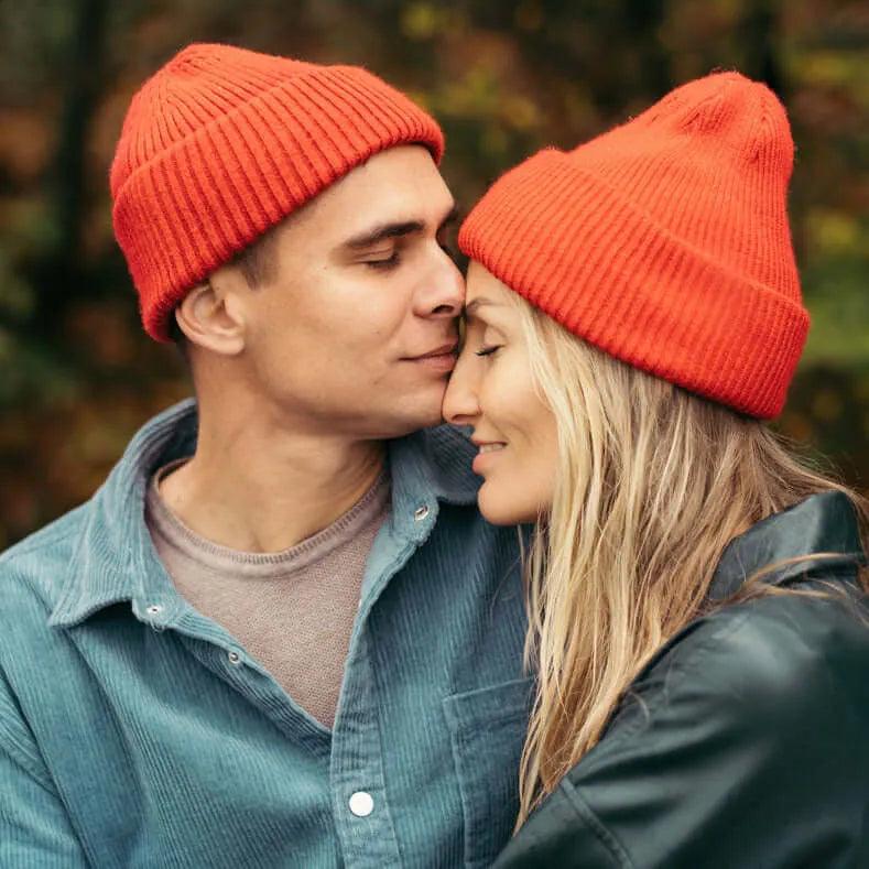 Paar mit roten Mützen kuschelt im Freien, Herbstkleidung, Liebe, Natur