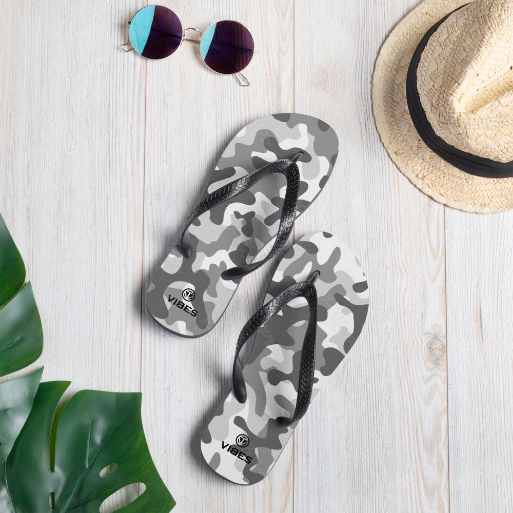 VIBES Flip Flops grau Camouflage auf hellem Holz, mit Sonnenbrille, Strohhut und Monstera-Blatt
