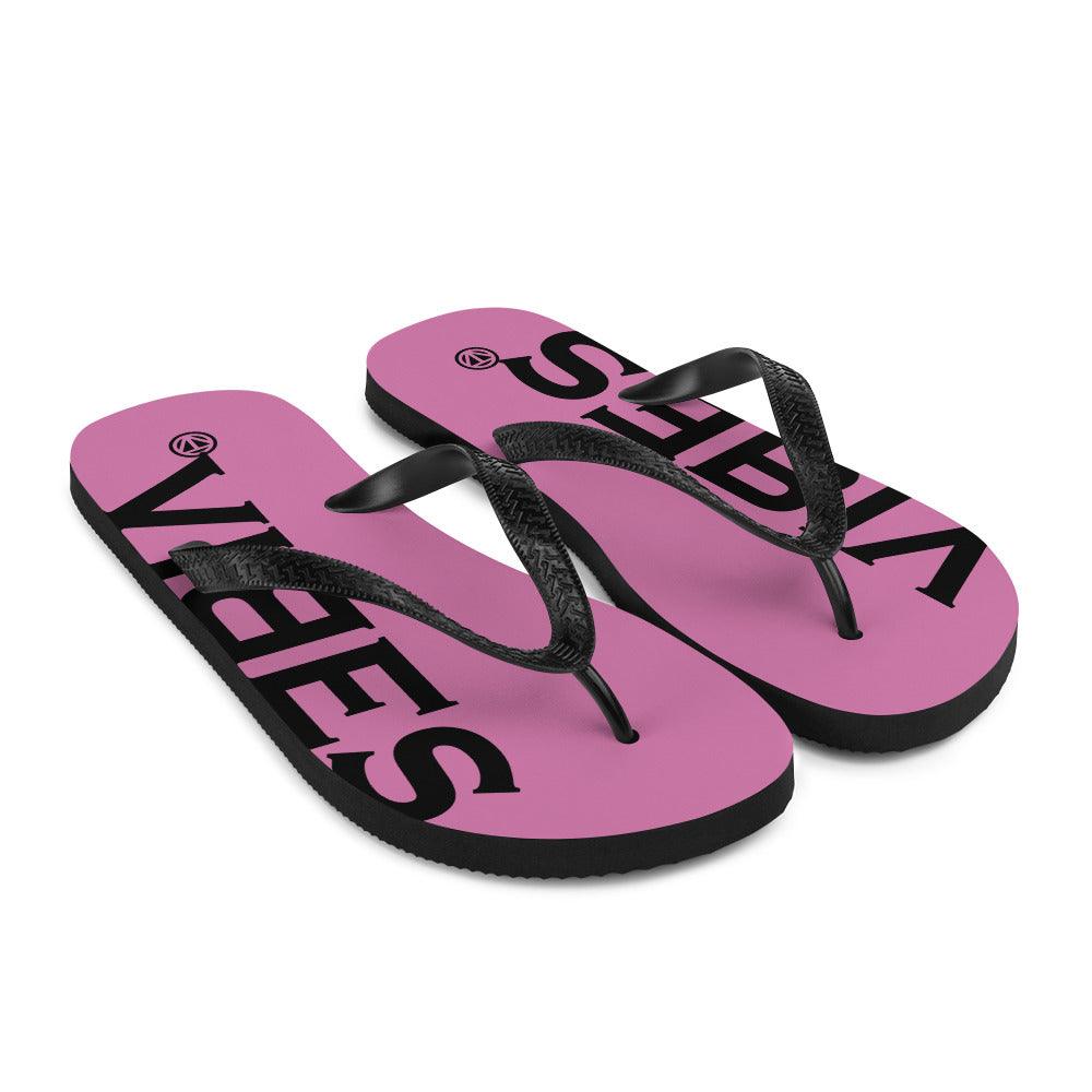 Pink Flip Flops mit schwarzem Vibes Schriftzug und schwarzen Riemen auf weißem Hintergrund