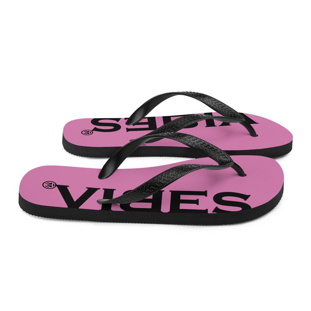 Pink Flip-Flop Sandalen mit schwarzem Vibes-Print und schwarzen Riemen auf weißem Hintergrund