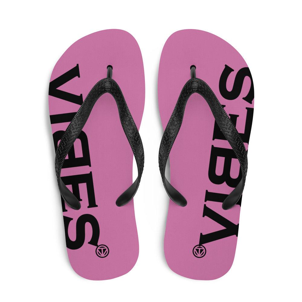 Pink Flip-Flops mit schwarzem VIBES Schriftzug und schwarzen Riemen auf weißem Hintergrund