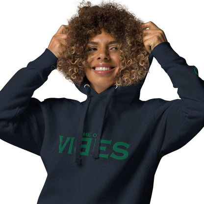 Frau mit lockigen Haaren trägt marineblauen Hoodie mit grünem Vibes Schriftzug, lächelt