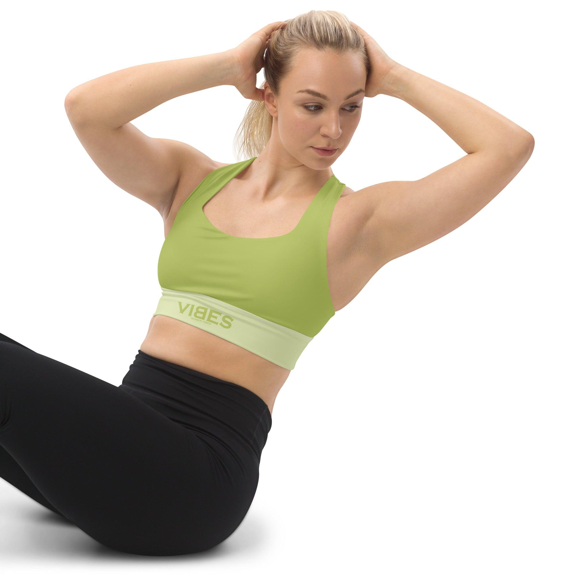 Frau trägt grünen VIBES Sport-BH und schwarze Leggings beim Workout auf weißem Hintergrund