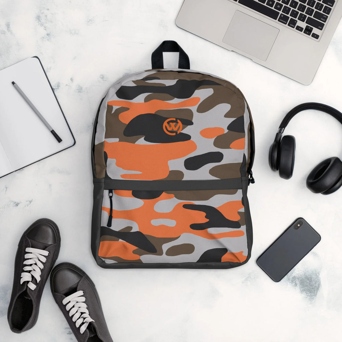 CREWILD Rucksack im orangefarbenen Camouflage-Design mit Laptop, Kopfhörern und Sneakern.