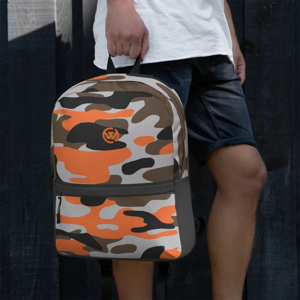 Person hält einen CREWILD Rucksack mit orange-grauem Camouflage-Muster vor dunklem Hintergrund.
