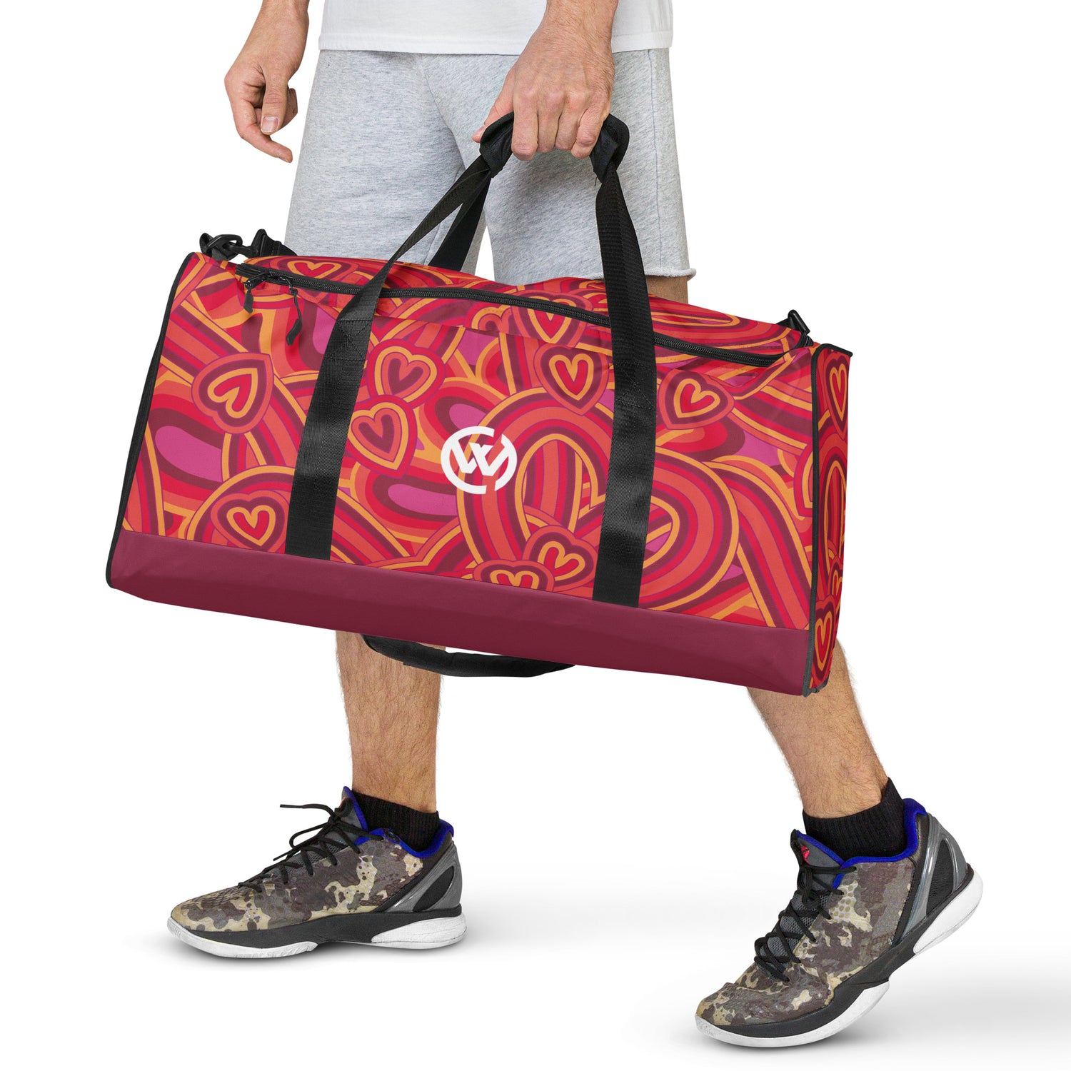 Person trägt eine sportliche Reisetasche mit buntem Herzmuster und Logo.