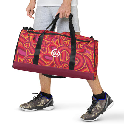 Person trägt eine sportliche Reisetasche mit buntem Herzmuster und Logo.
