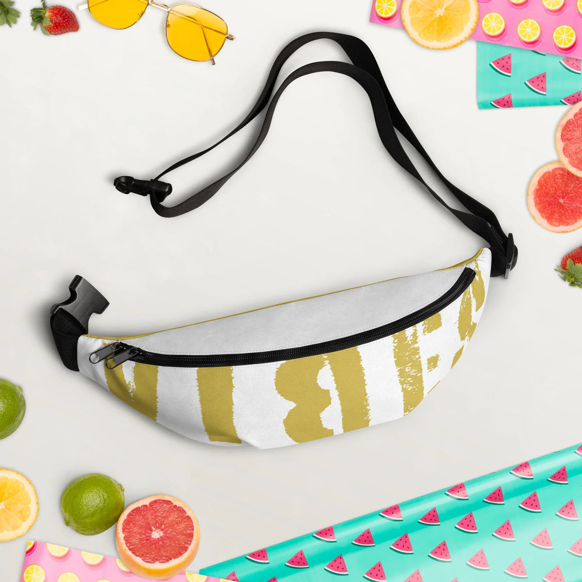 Weiße Bauchtasche mit gelbem Grafikprint, umgeben von Sommerfrüchten und einer Sonnenbrille.