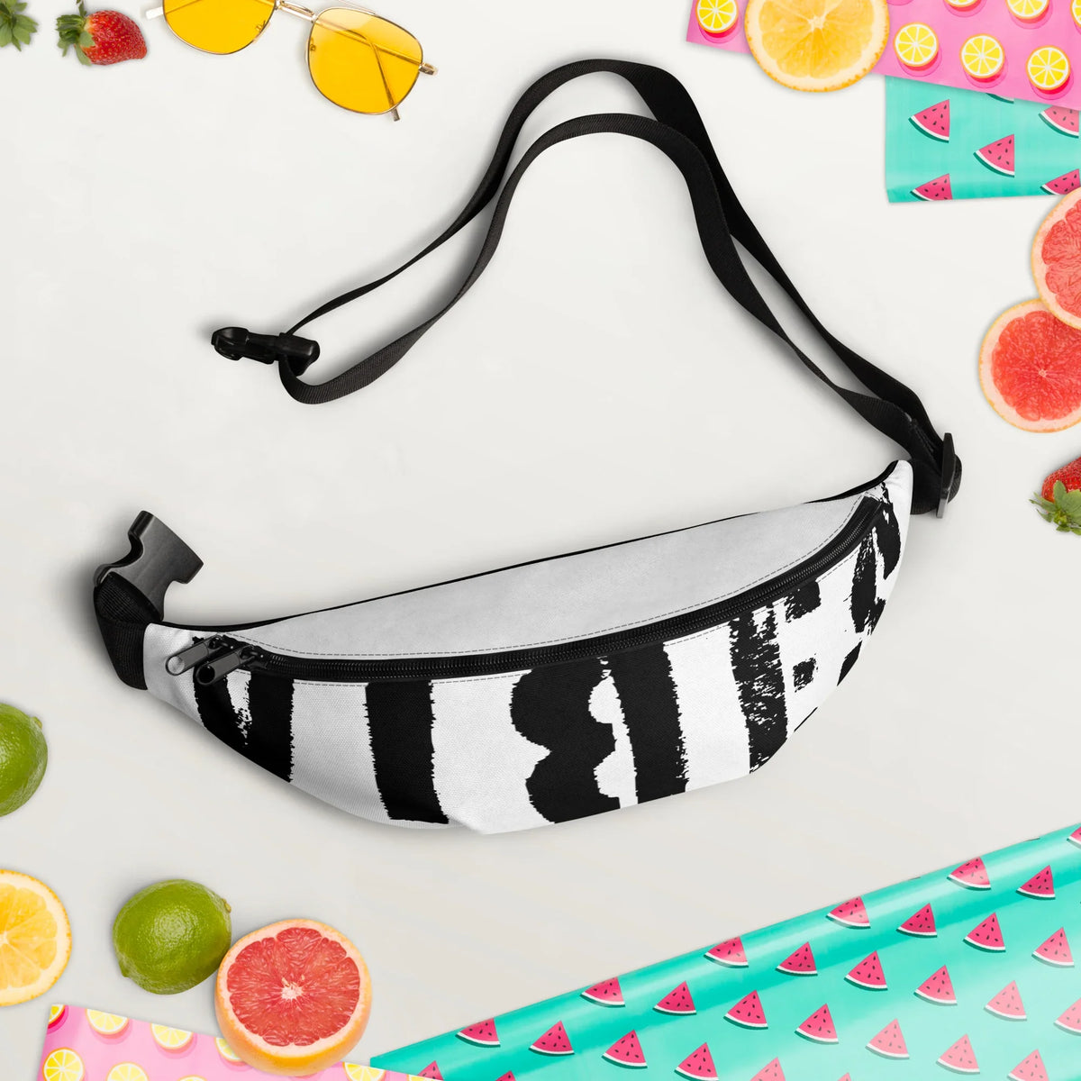 Schwarz-weiße Gürteltasche mit abstraktem Muster, umgeben von Sommerfrüchten und Accessoires
